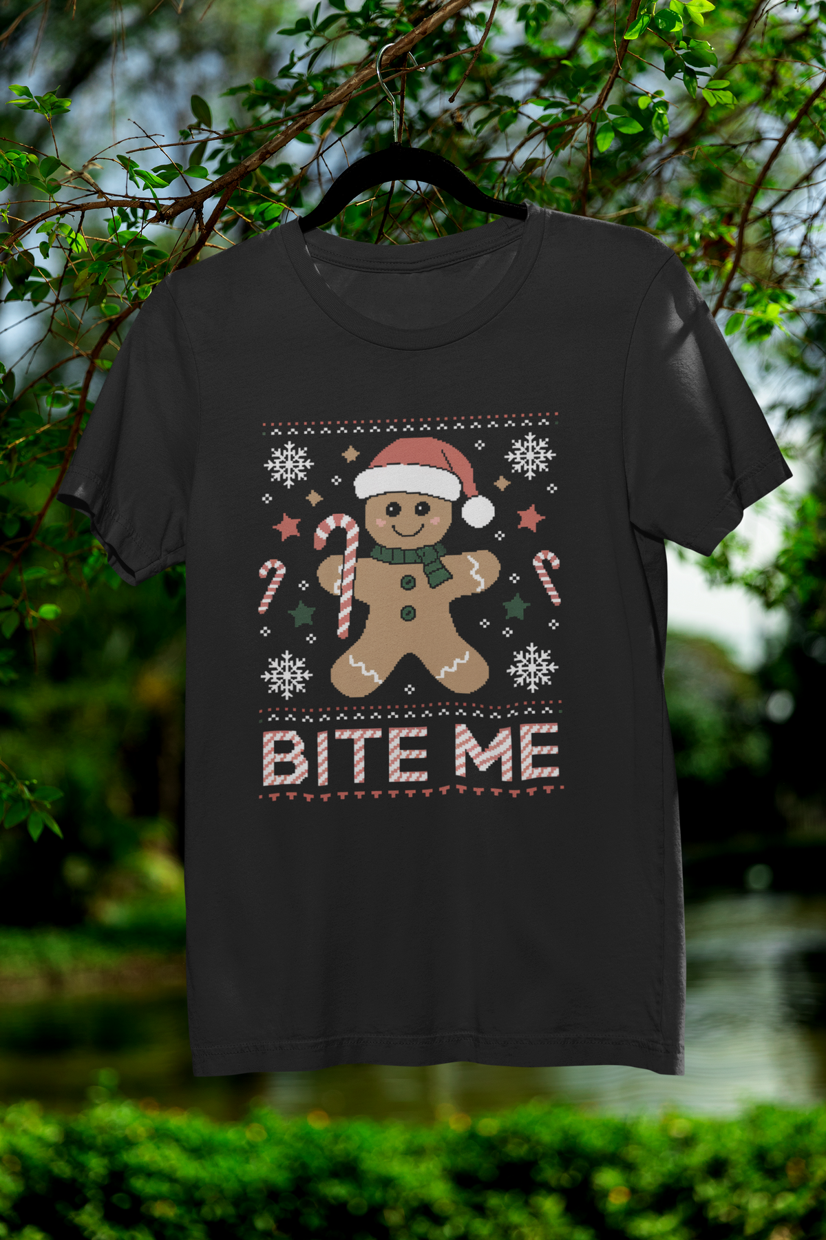 'Bite Me' gingerbread man t-shirt in black, hanging outdoors in a garden, funny Christmas gift shirt