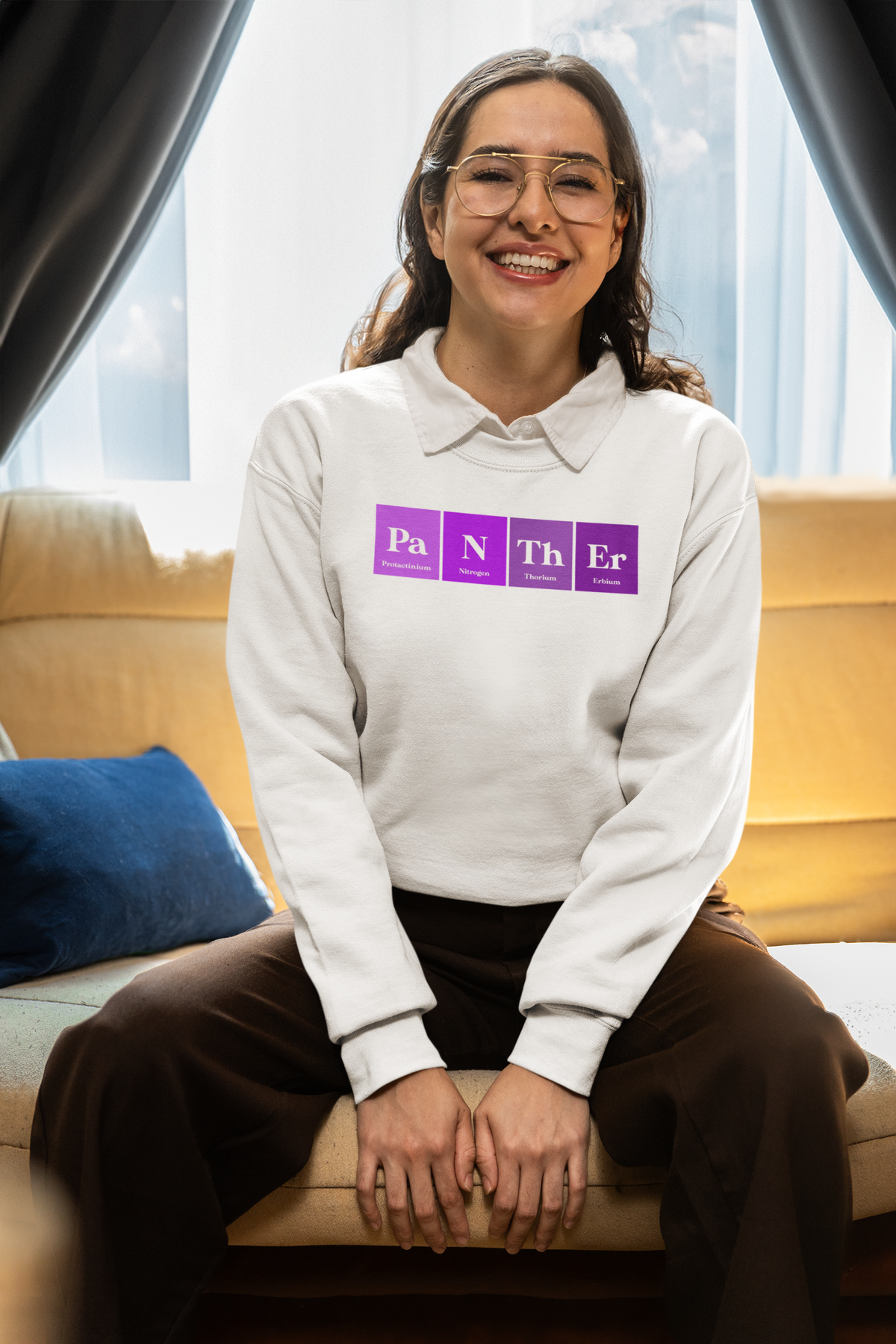 'Pa-N-Th-Er' periodic table sweatshirt in white, woman sitting on a couch wearing it, cozy lifestyle photo