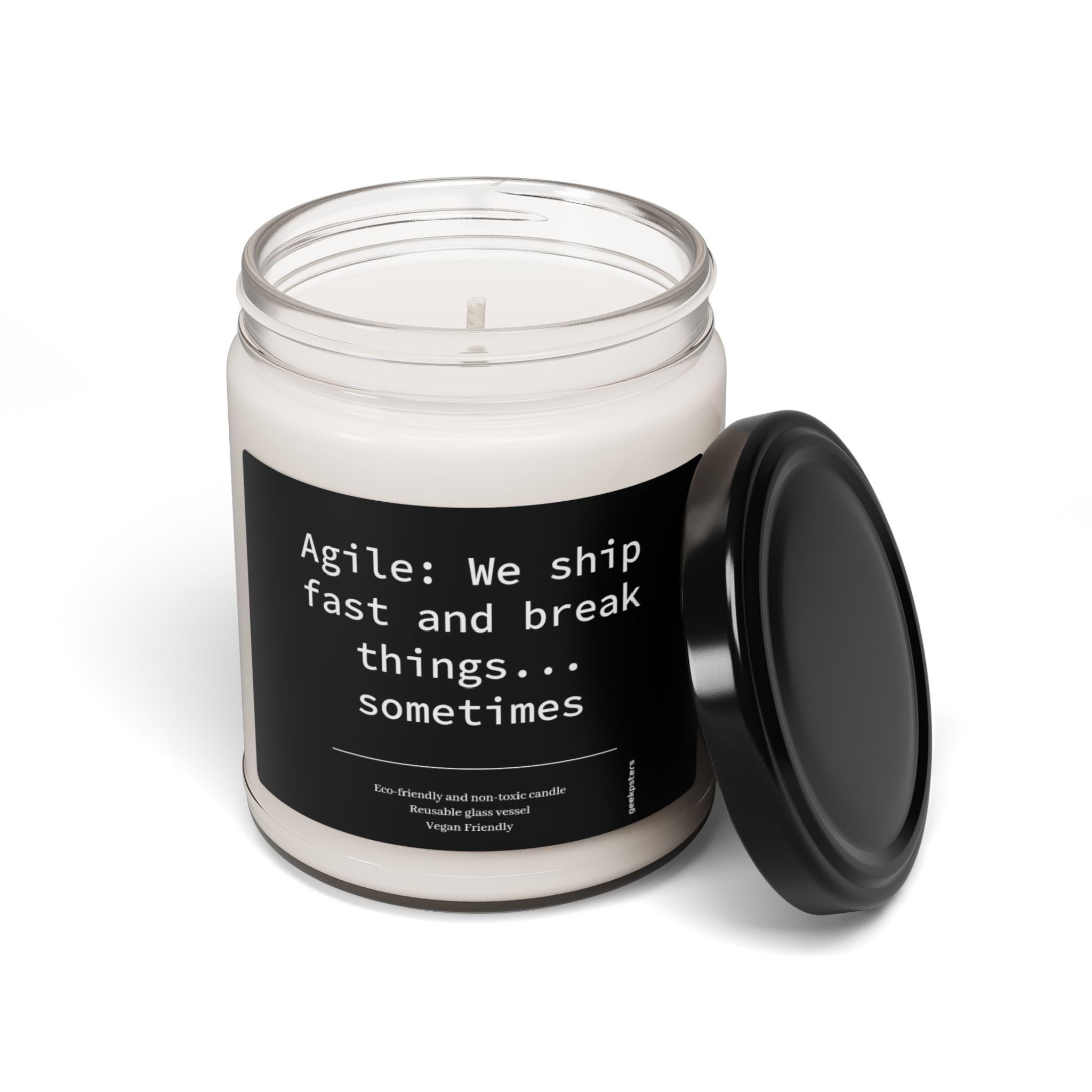 The "Agile: We Ship Fast and Brake Things" 9oz geek candle features a white soy blend in a glass jar with a black lid removed, labeled with "Agile: We ship fast and break things... sometimes." Made eco-friendly and vegan.