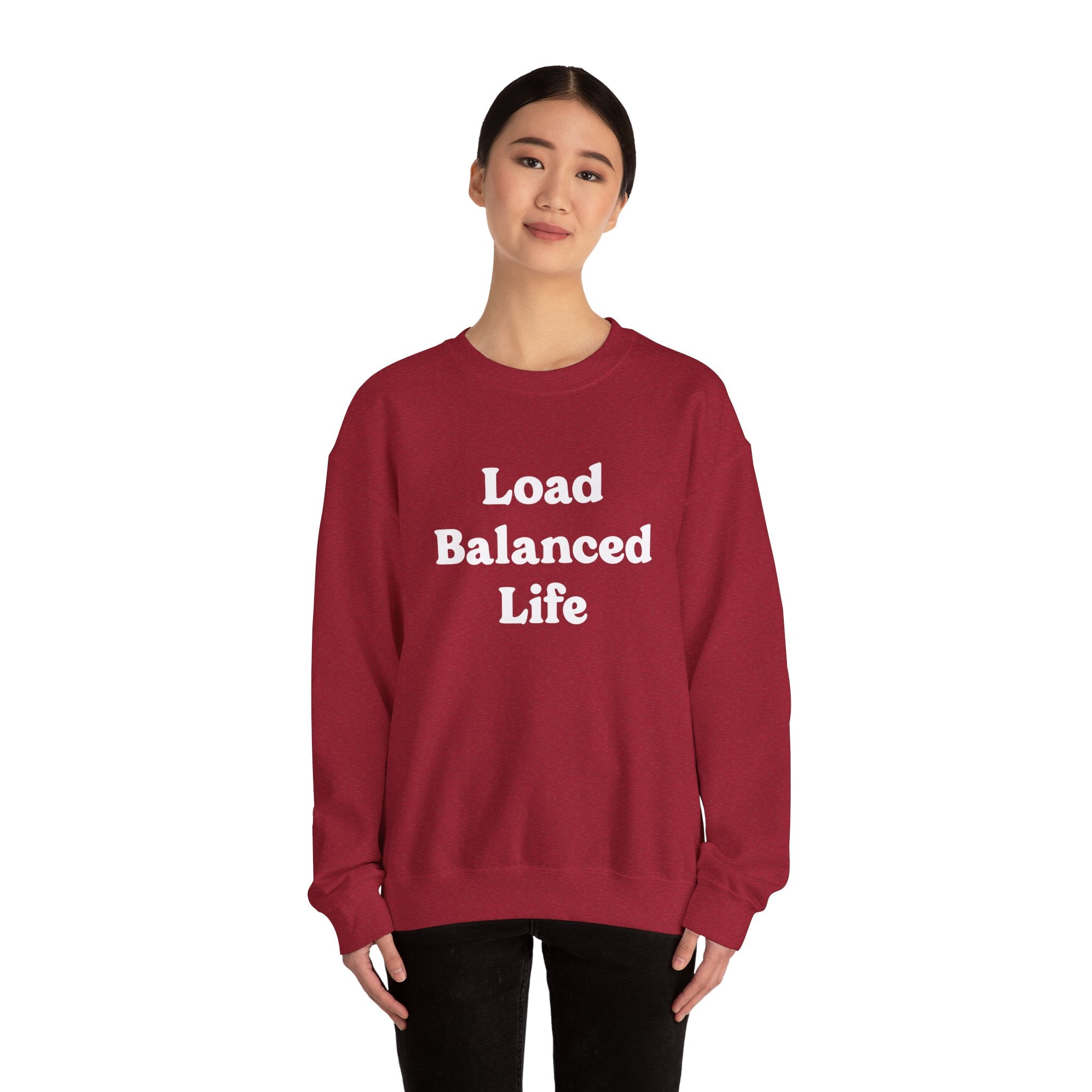 A person relishes cozy comfort while wearing the "Load Balanced Life" maroon sweatshirt, standing against a pristine white background.