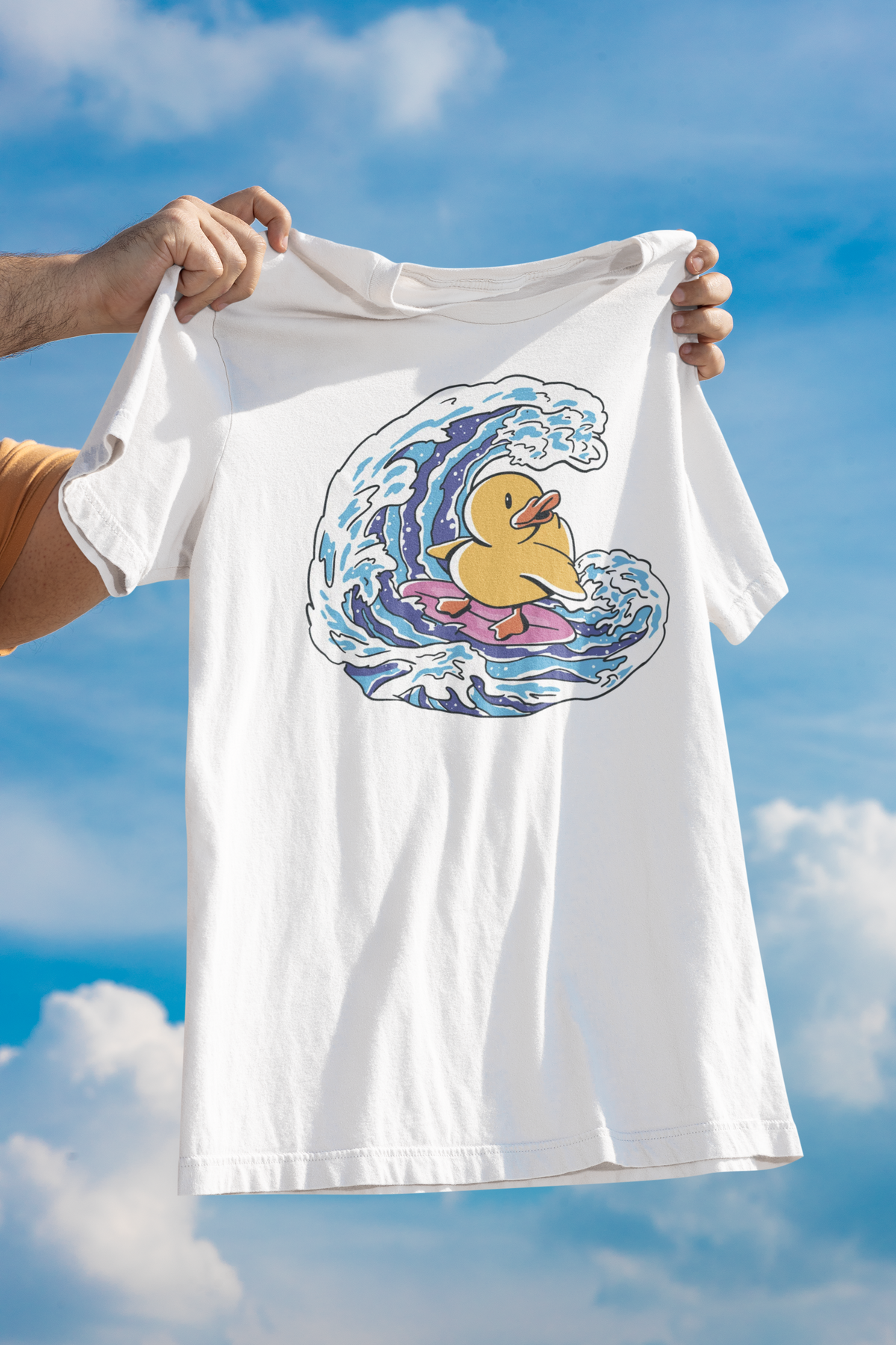 Surfing duck t-shirt in white, held up outdoors against a cloudy sky backdrop, funny beach duck gift
