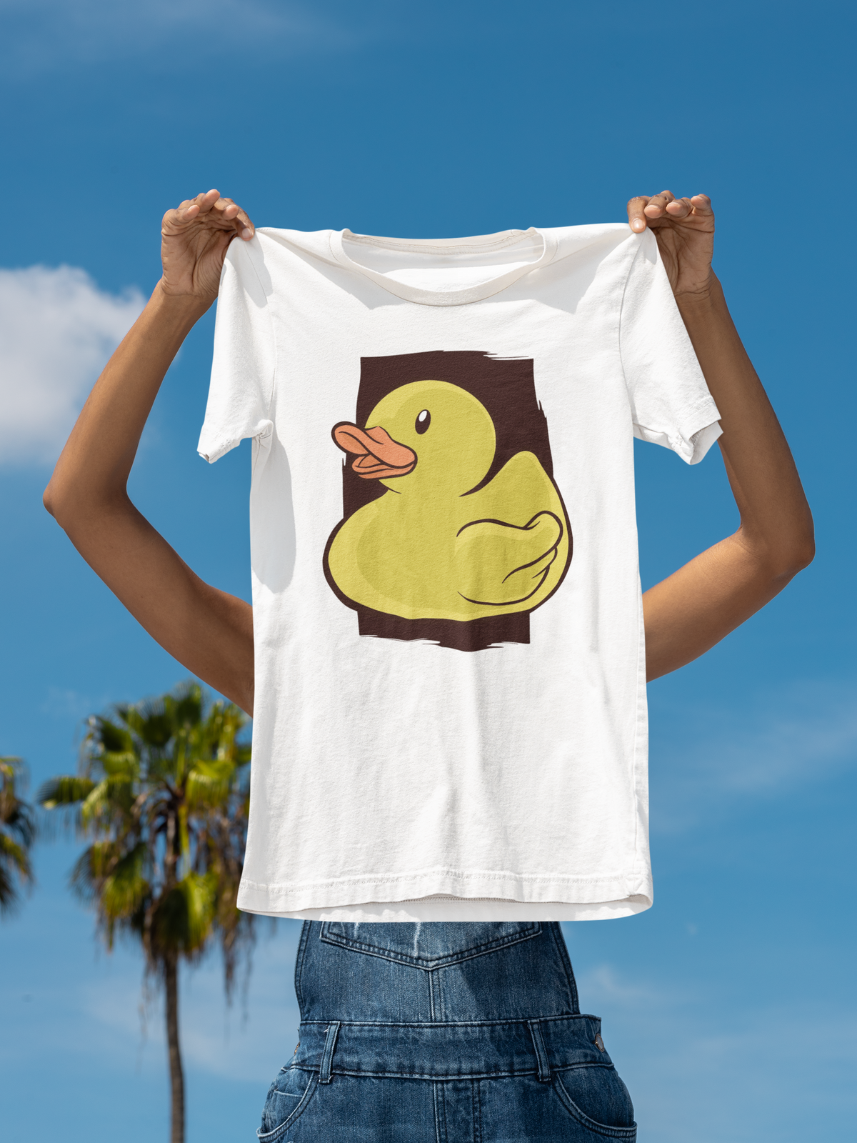 Classic rubber duck t-shirt in white, held up outdoors against a palm tree sky backdrop, funny animal lover gift