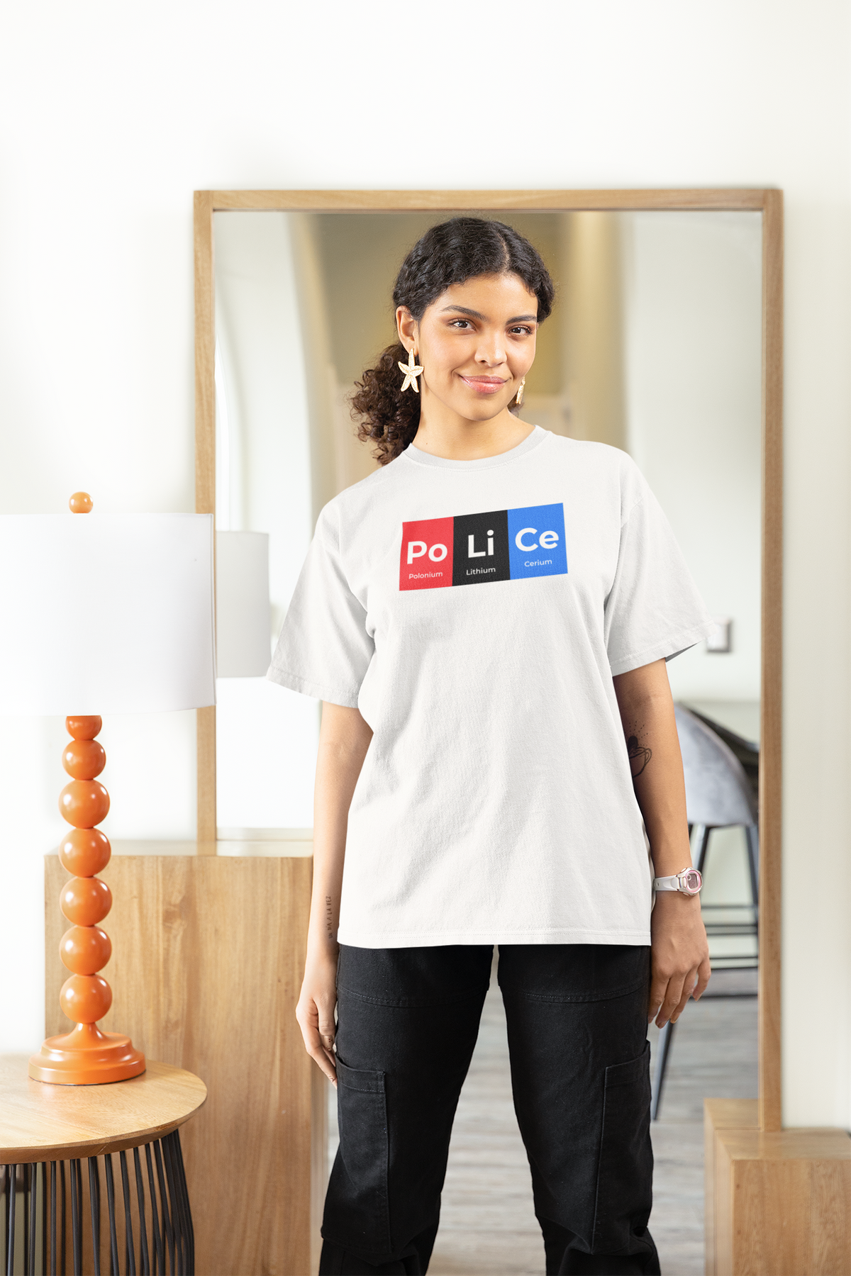 'Po-Li-Ce' periodic table women's tee in white, woman standing at home, casual lifestyle photo