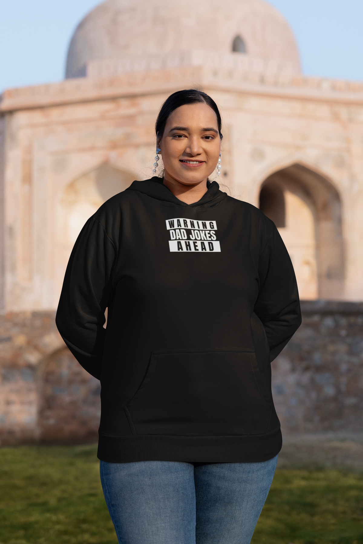 'Warning Dad Joke Ahead Hoodie' in black, woman at a historic monument, Hoodie mockup, Geekpsters