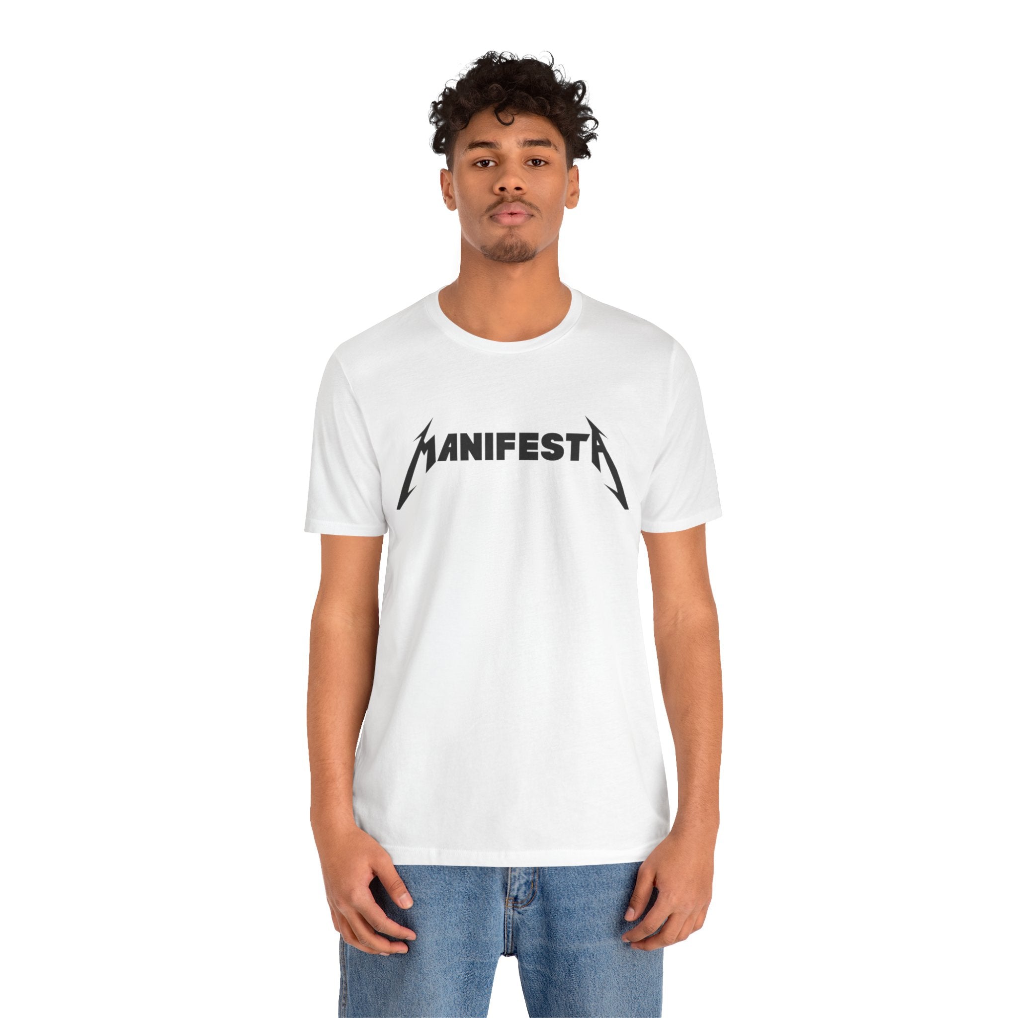 A man with curly hair wears a Manifesta Tee Shirt paired with blue jeans, standing against a plain white background, highlighting the essence of a geeky wardrobe.