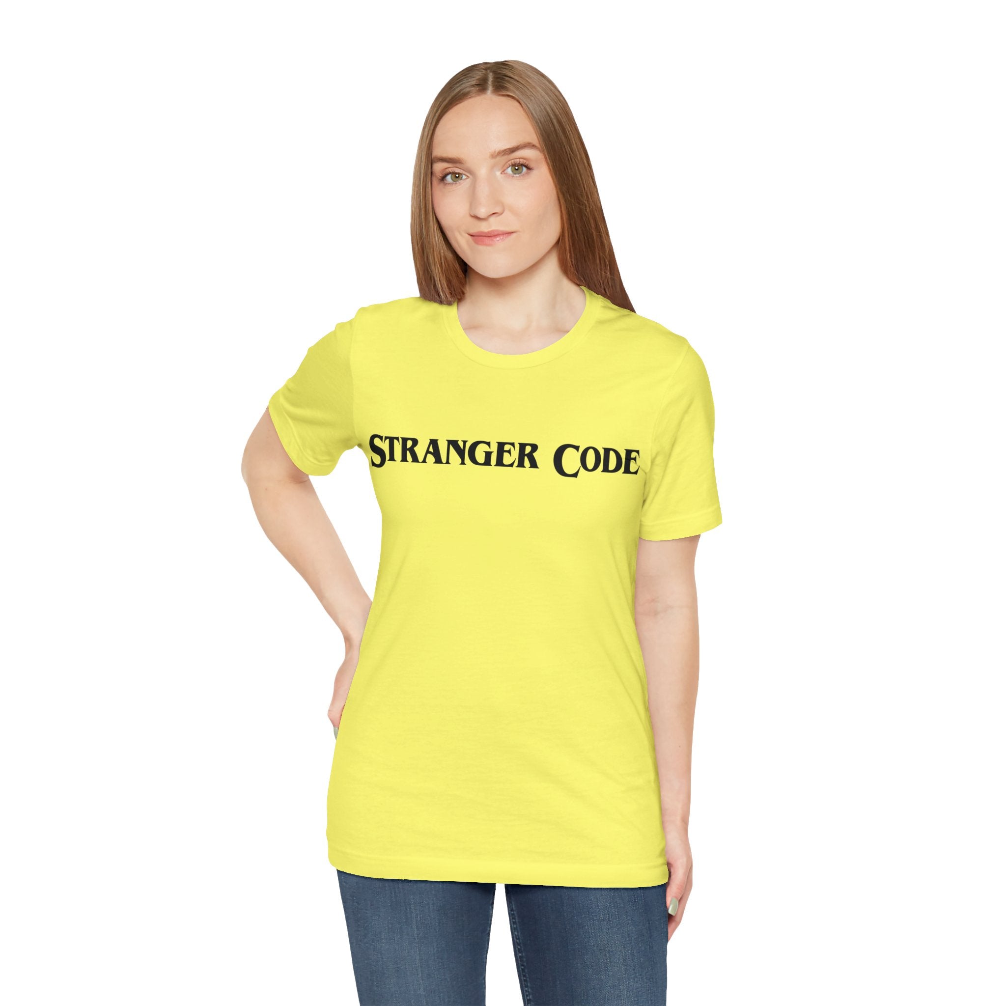 A person is seen against a plain white background, wearing a Stranger Code Tee Shirt made from soft cotton in a vibrant yellow shade with "STRANGER CODE" printed on the front. This classic unisex jersey tee offers both comfort and style with its high-quality print.