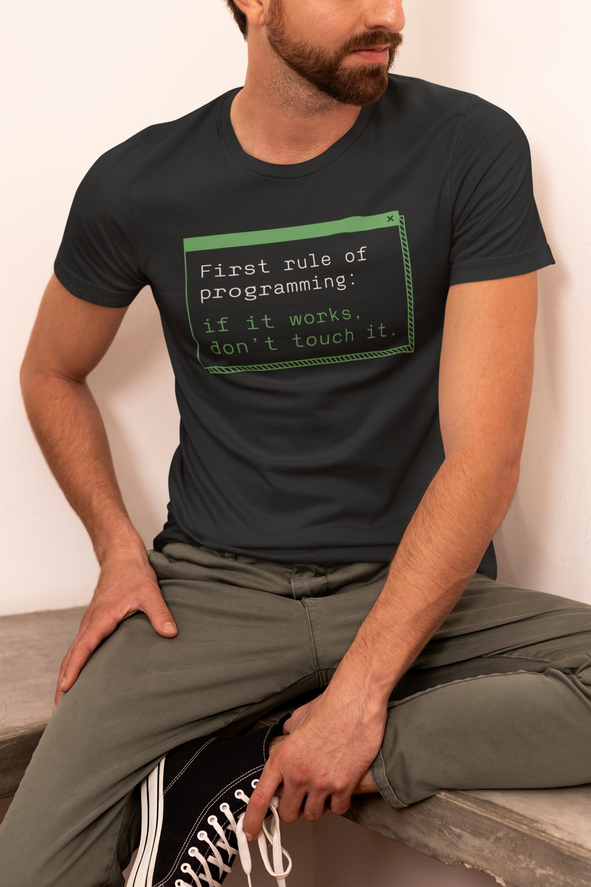 'First Rule of Programming' t-shirt in black, man model wearing it seated on a wooden bench