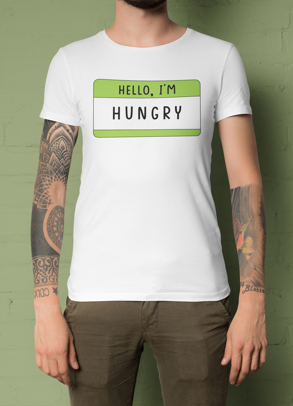 Hello I'm Hungry name tag T-shirt in white, tattooed man wearing it, green backdrop, foodie gift tee