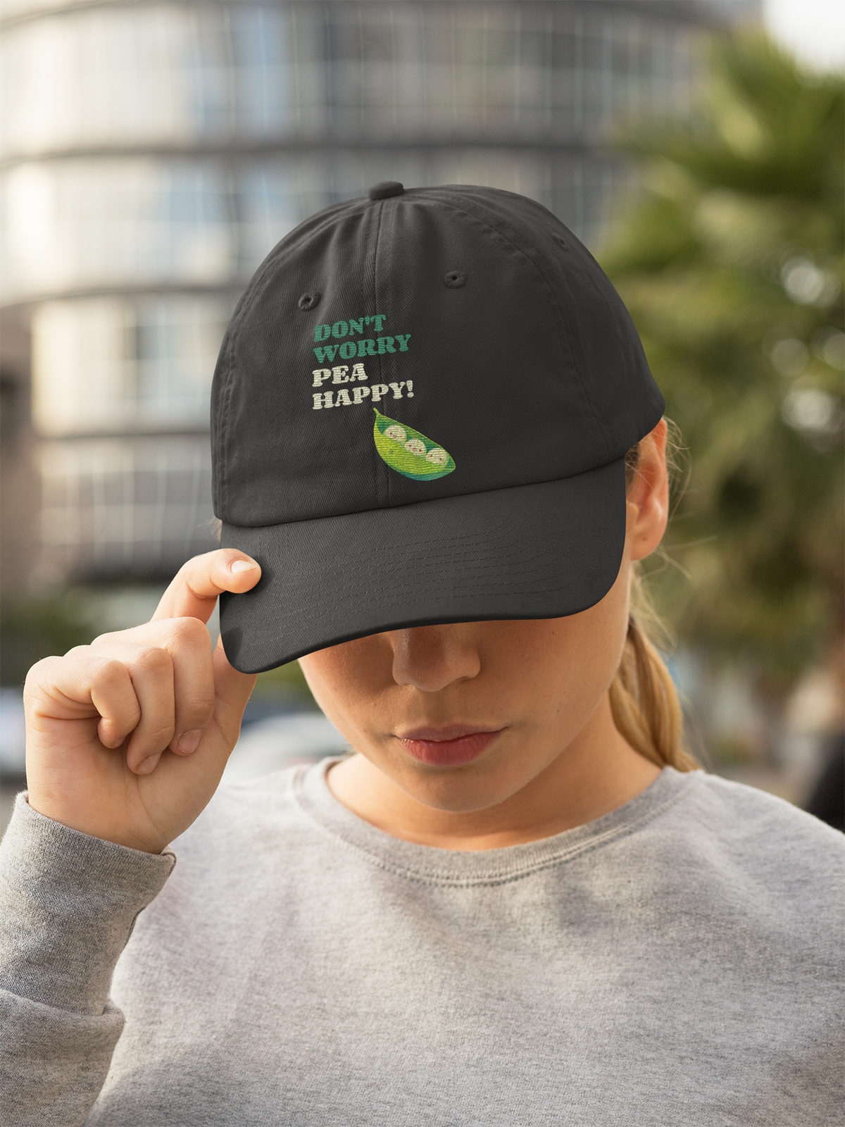 'Don't Worry Pea Happy' pea pun dad hat in black, woman wearing it outdoors, funny vegetable gift