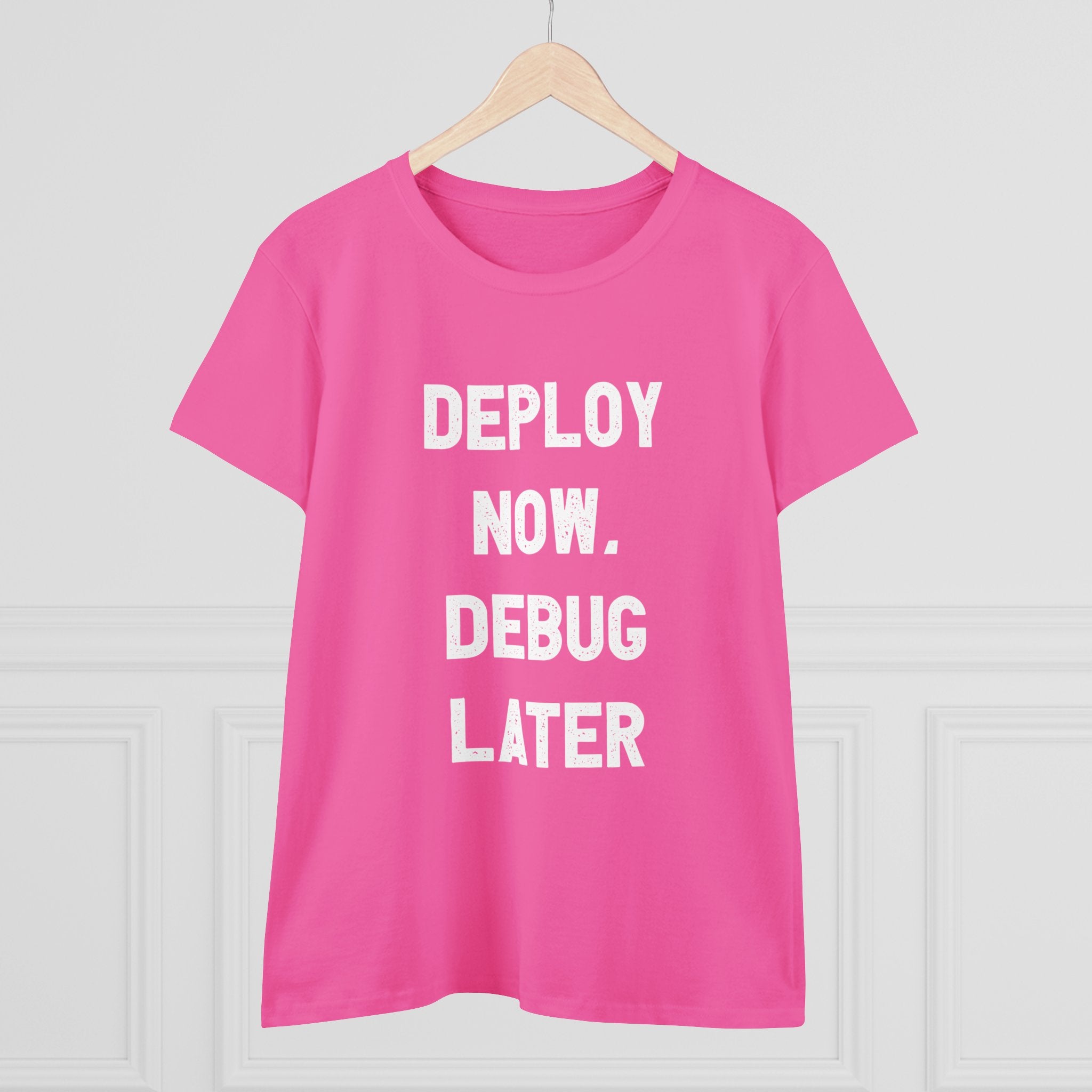 The Women's Tee "Deploy Now, Debug Later" is made from premium cotton and elegantly showcases the slogan "DEPLOY NOW. DEBUG LATER" printed in white, hanging confidently on a hanger.