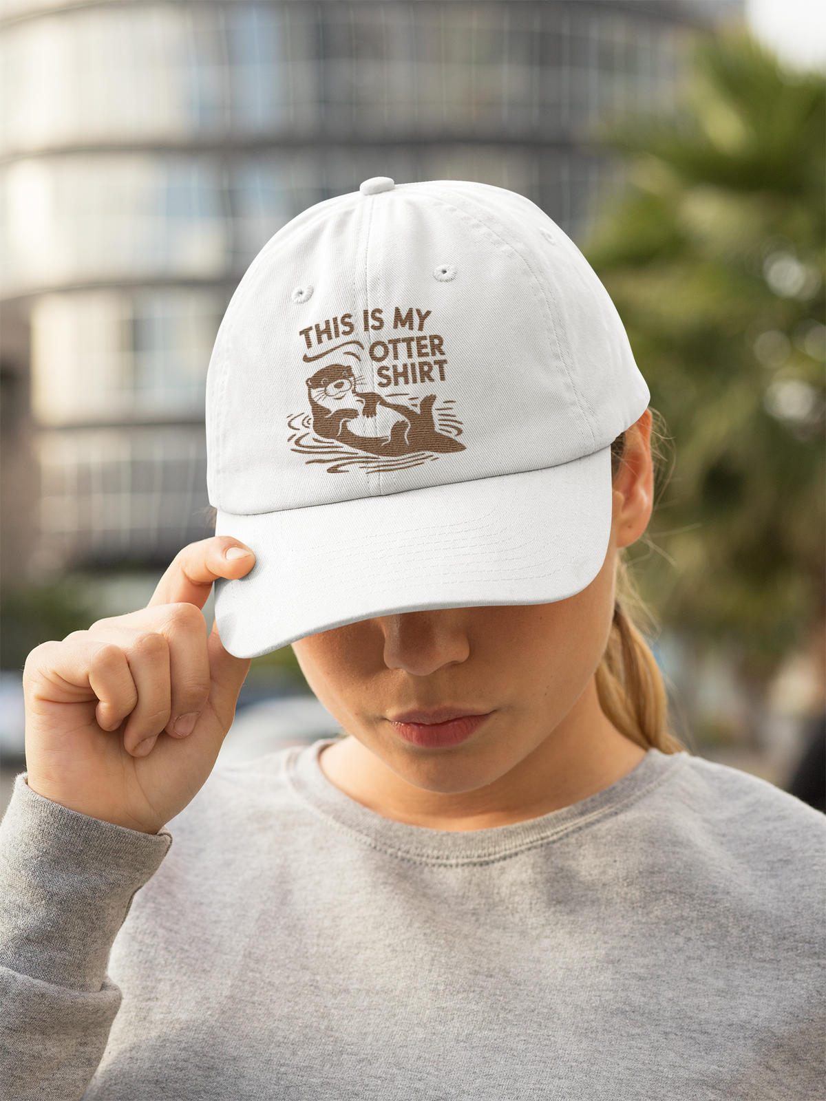'This Is My Otter Shirt' cap in white, woman wearing it outdoors in the city, funny animal pun gift