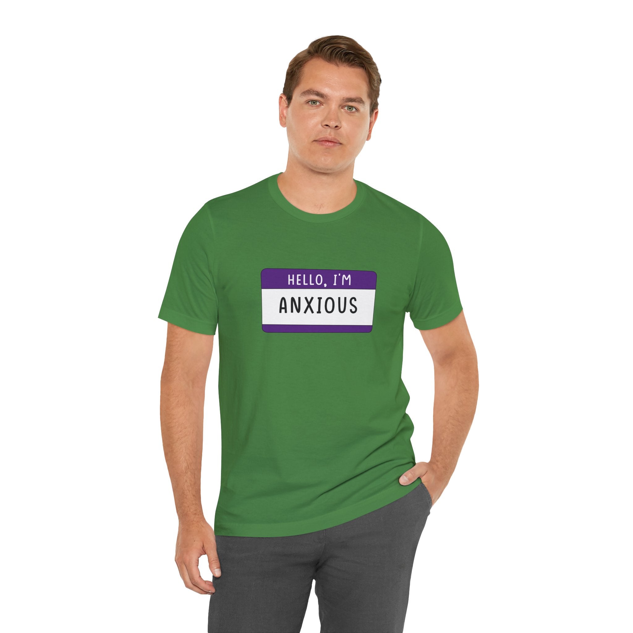 A person confidently wears the "Hello, I'm Anxious" T-shirt in green, featuring a cheerful nametag design.