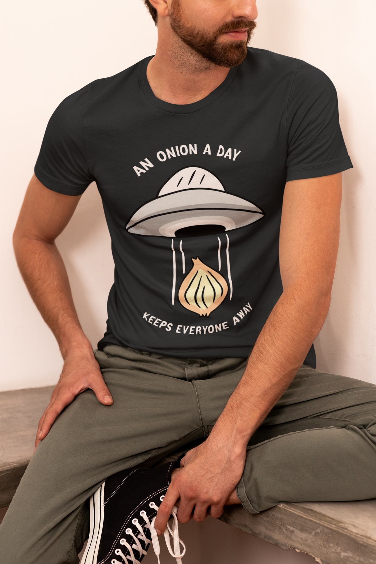 'An Onion a Day Keeps Everyone Away' UFO t-shirt in black, man wearing it seated, funny alien gift