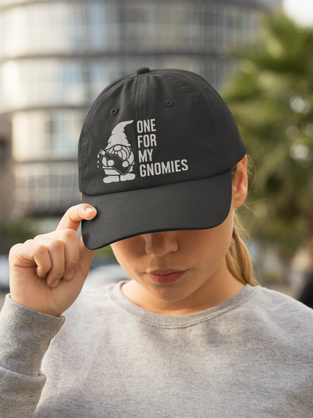 One For My Gnomies cap in black, woman wearing it outdoors in the city, funny gnome pun gift