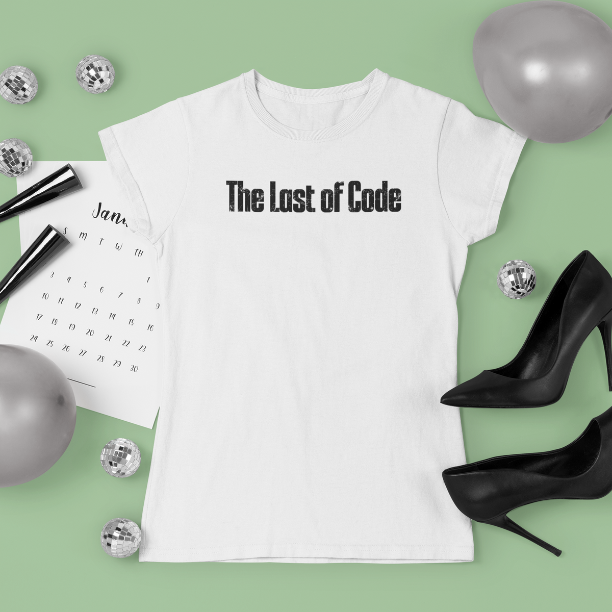 'The Last of Code' T-shirt in white, flat lay styled with dice and heels on green background, gift tee