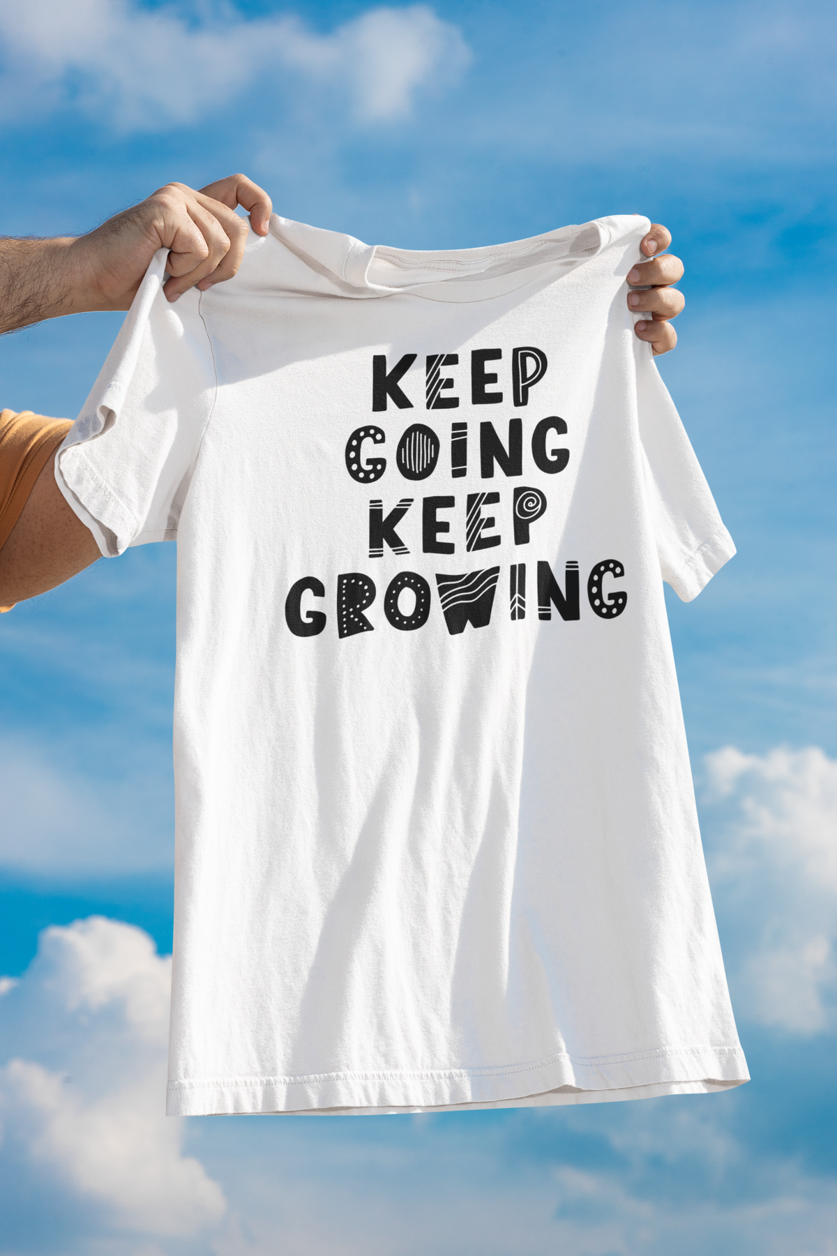 'Keep Going Keep Growing' t-shirt in white, held up against a blue sky