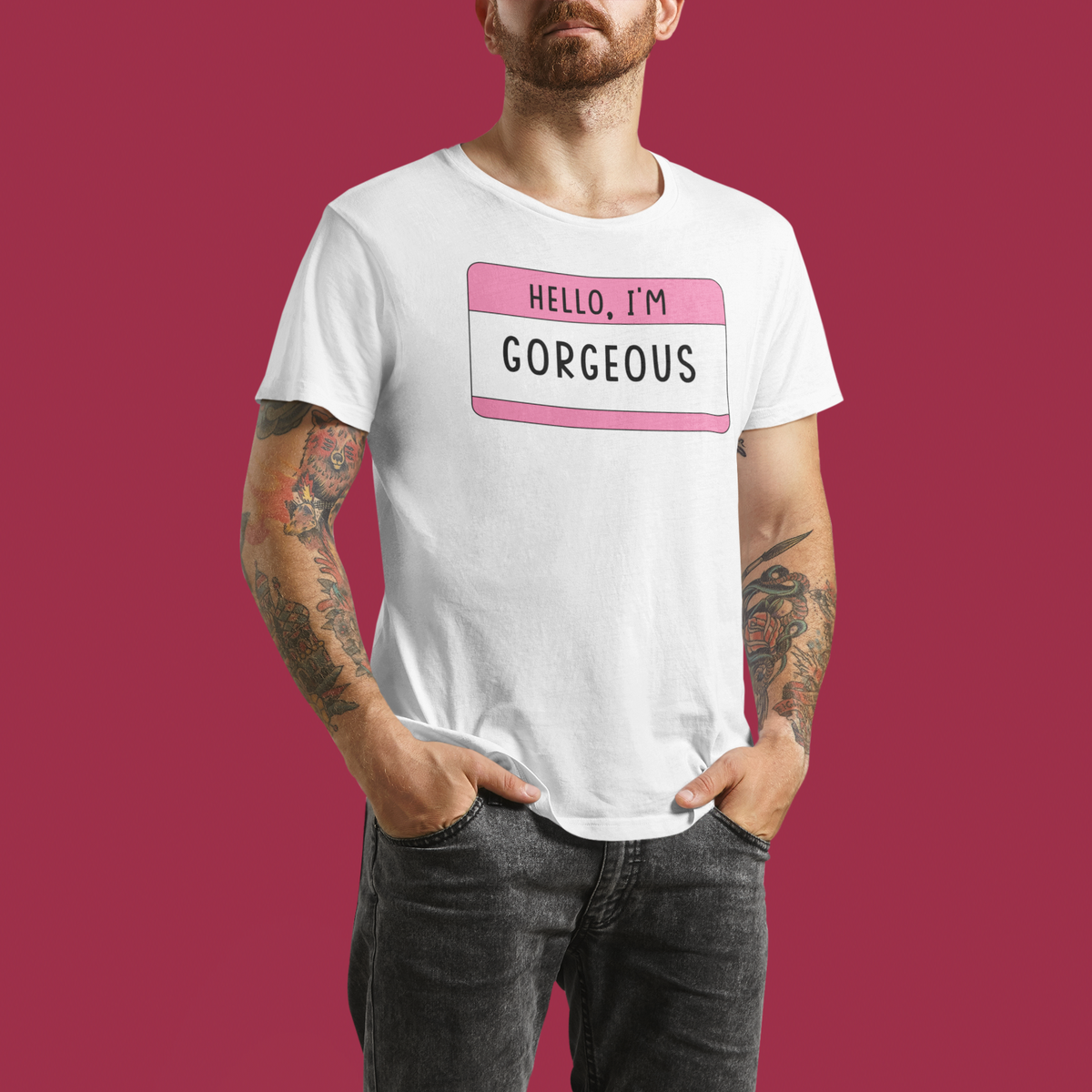 Hello I'm Gorgeous name tag T-shirt in white, tattooed man wearing it, maroon backdrop, gift tee