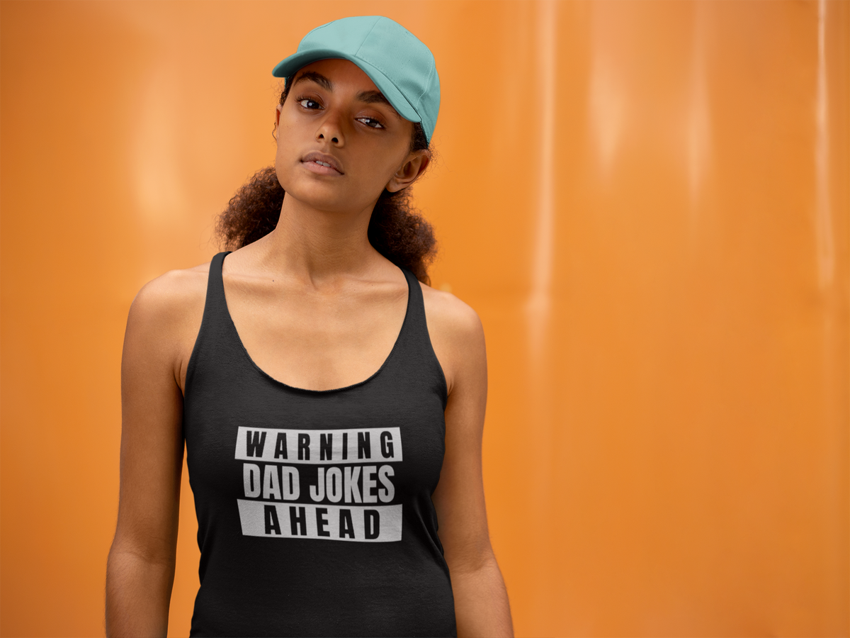 'Warning Dad Joke Ahead' racerback tank top in black, woman wearing it by an orange wall, Tank Top mockup, Geekpsters