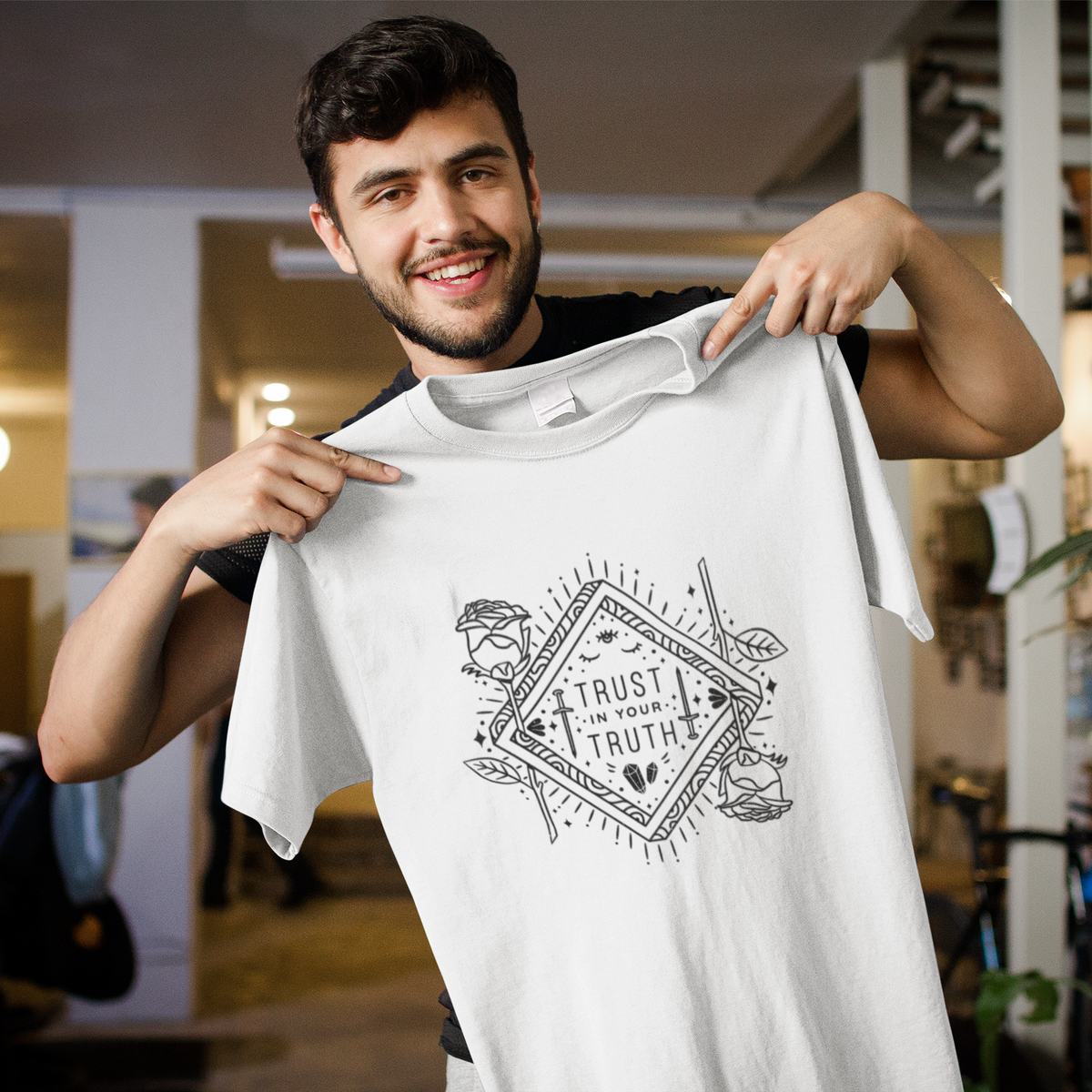 Trust in Your Truth t-shirt in white, man holding it up on a hanger in a cafe