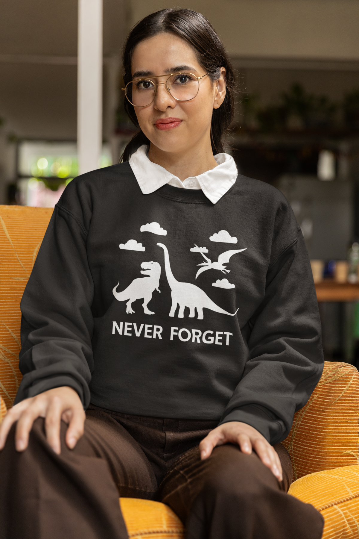 'Never Forget' dinosaur sweatshirt in black, woman wearing it seated indoors, funny paleontology gift