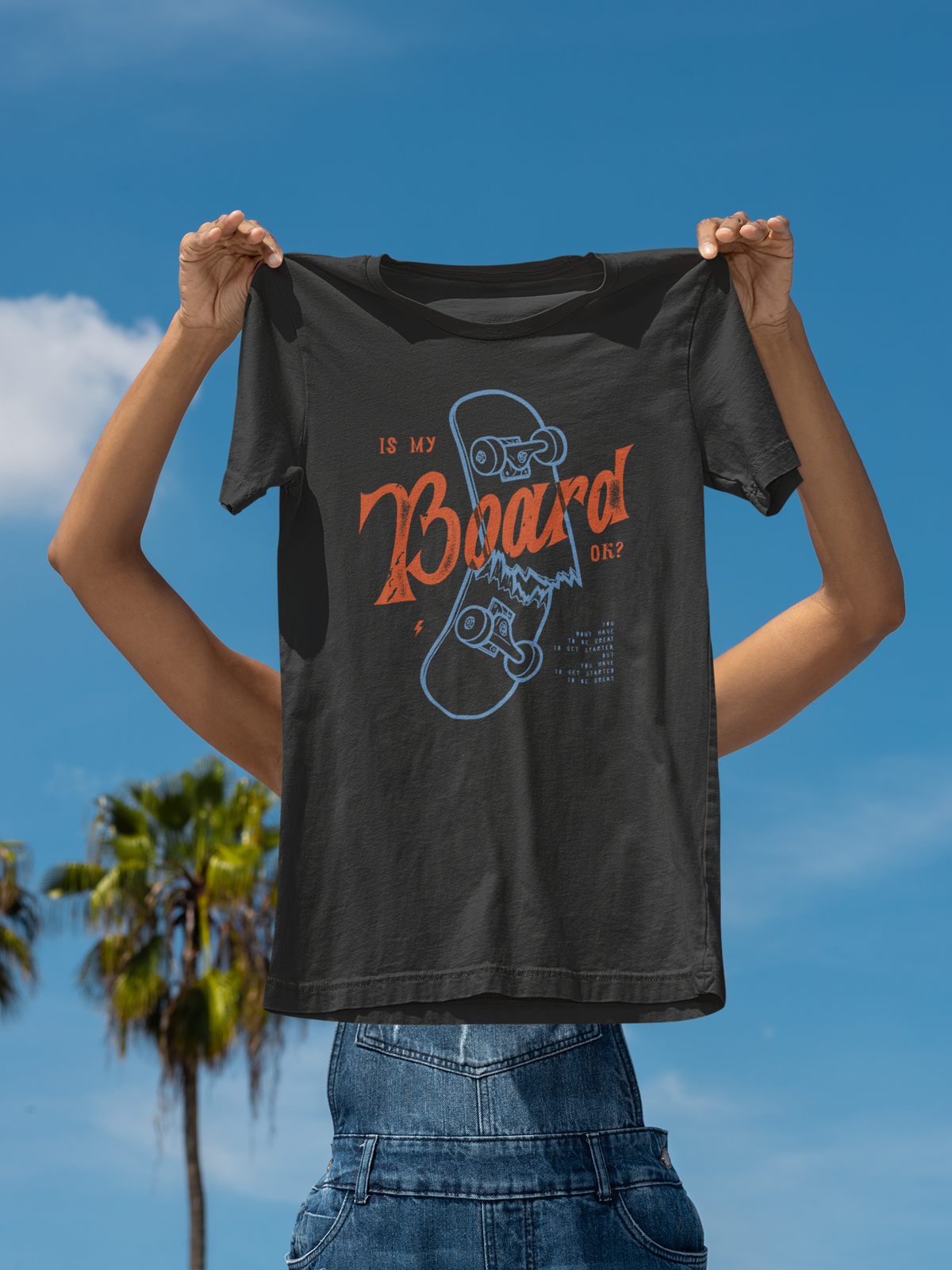 "Is My Board OK?" skateboard t-shirt in black, held up outdoors against sky, funny skater gift