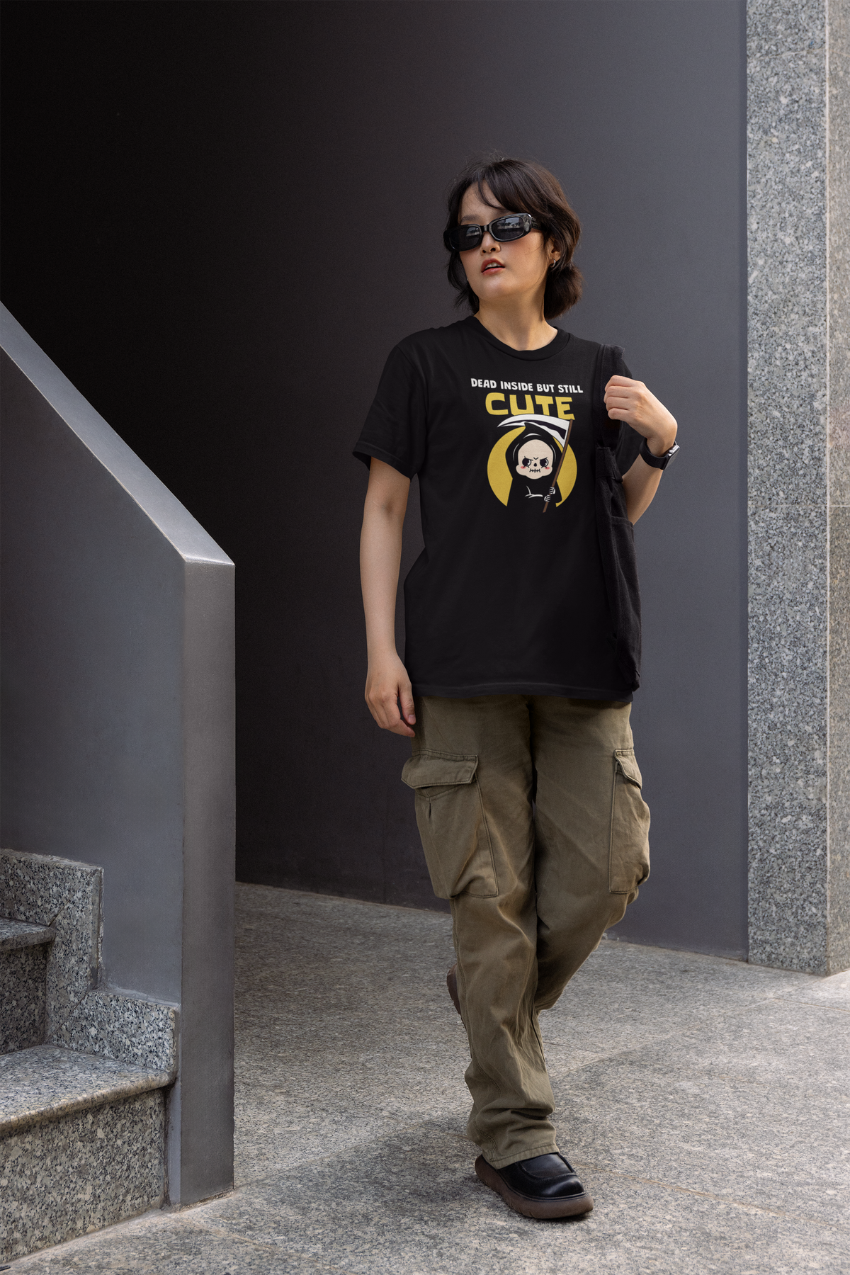 'Dead Inside but Still Cute' t-shirt in black, person wearing it outdoors on stairs, funny goth pun graphic gift