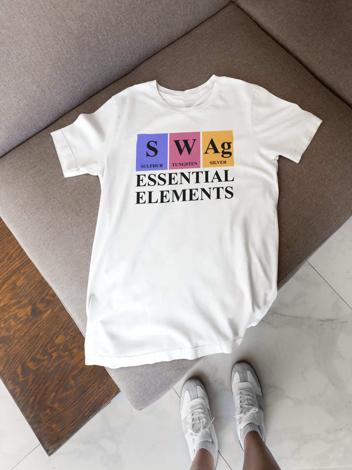 'SWAg Essential Elements' periodic table t-shirt in white, flat lay on wood floor, science teacher gift