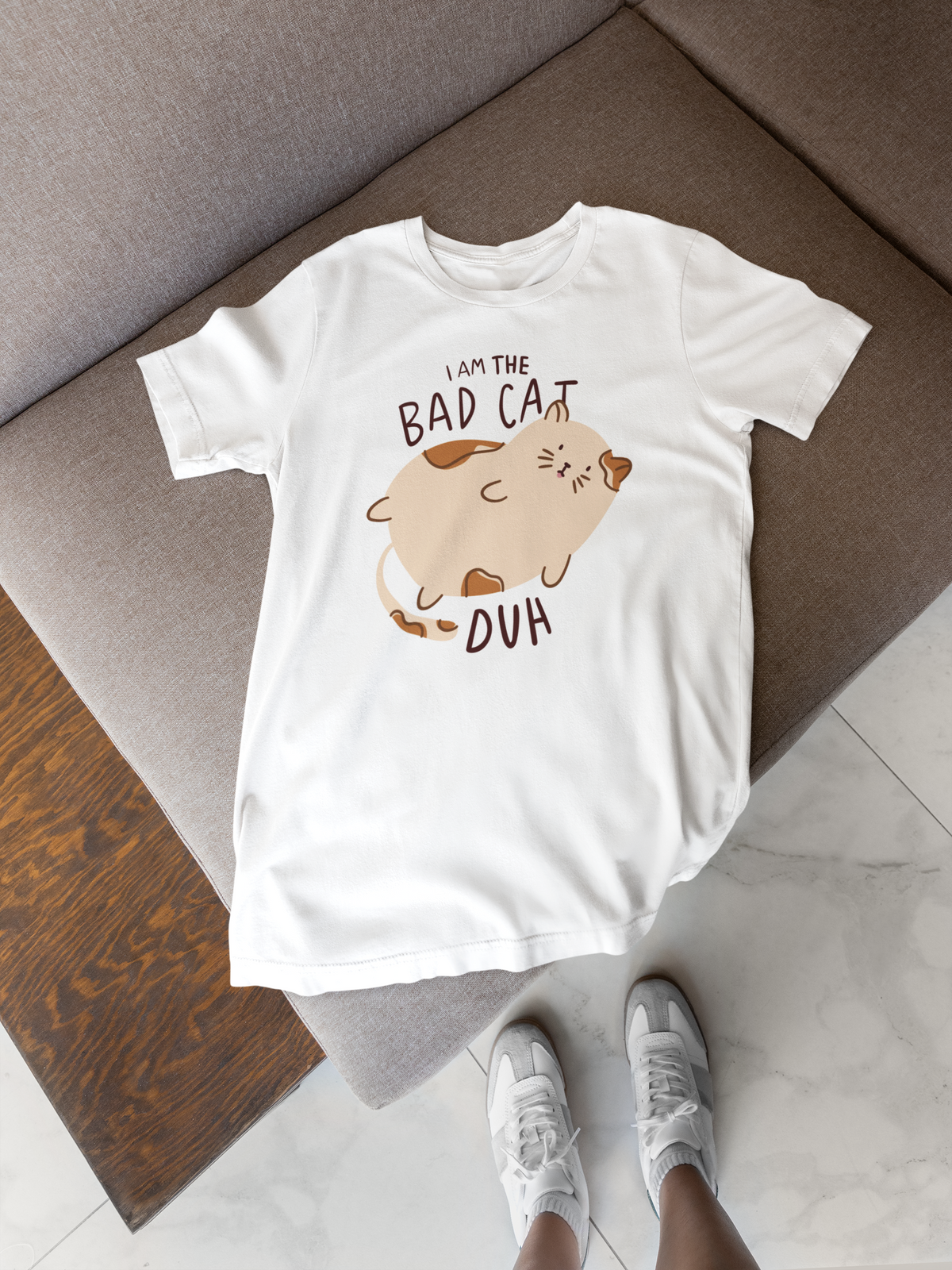 'I Am the Bad Cat Duh' T-shirt in white, flat lay on a wood floor, funny gift for cat owners