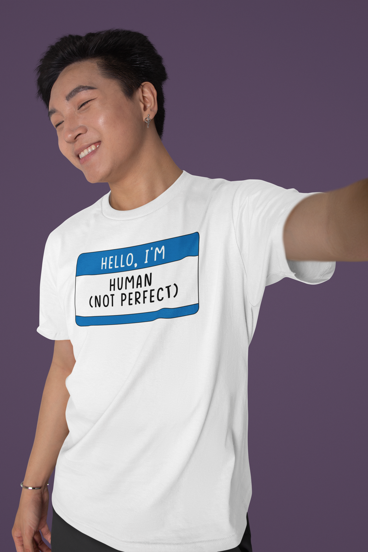 Hello I'm Human Not Perfect name tag T-shirt in white, man taking selfie against purple backdrop, gift tee