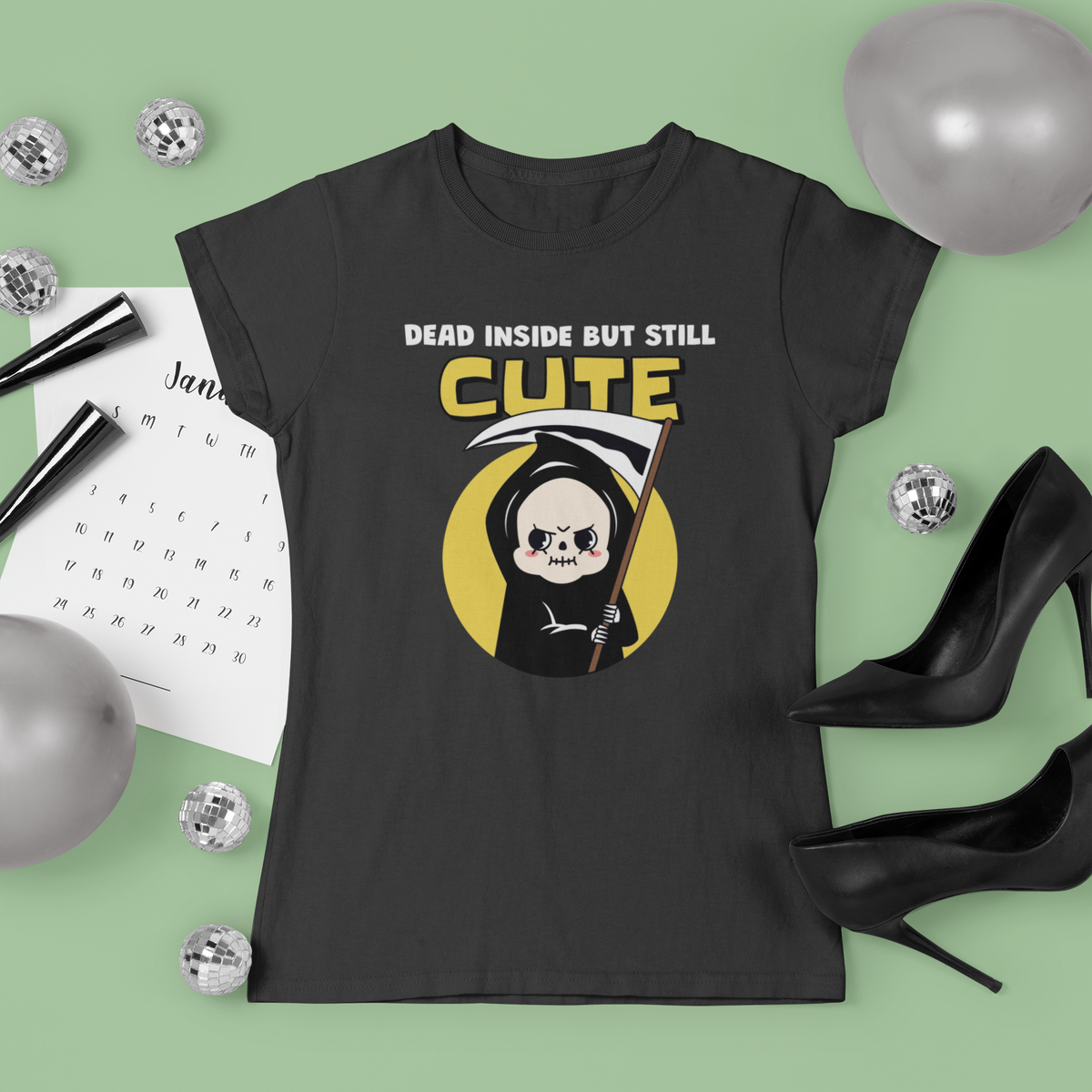 'Dead Inside but Still Cute' grim reaper t-shirt in charcoal, styled flat lay, green backdrop, gift