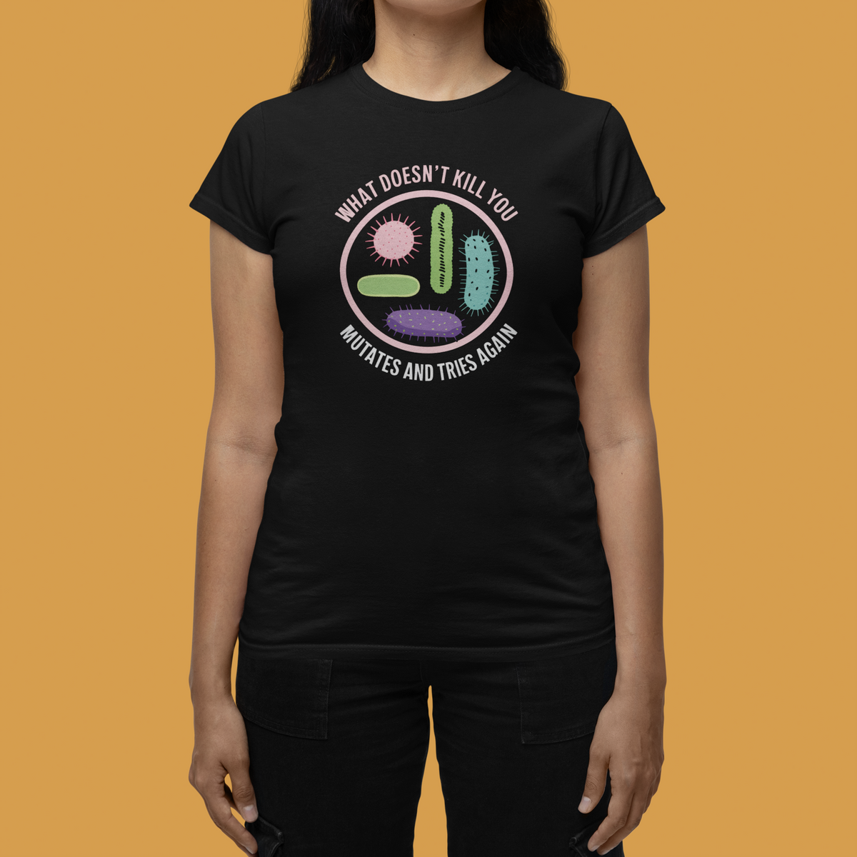 'What Doesn't Kill You' women's tee in black, close-up on woman, mustard backdrop, biology gift
