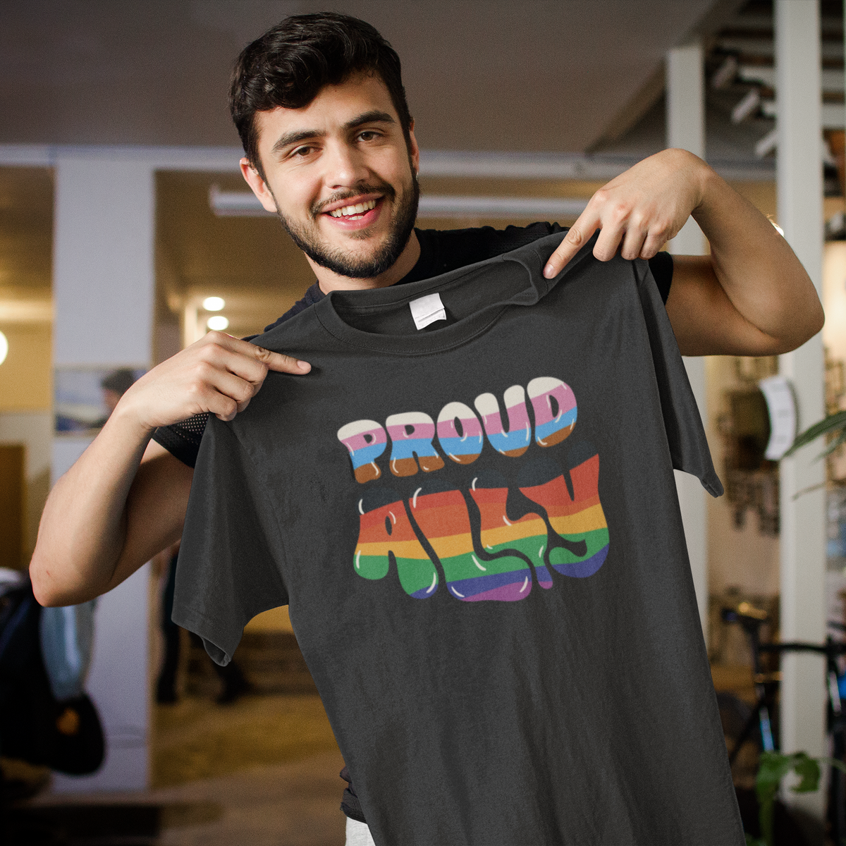 'Proud Ally' T-shirt in dark heather, man holding it up in a store, funny pride ally gift shirt
