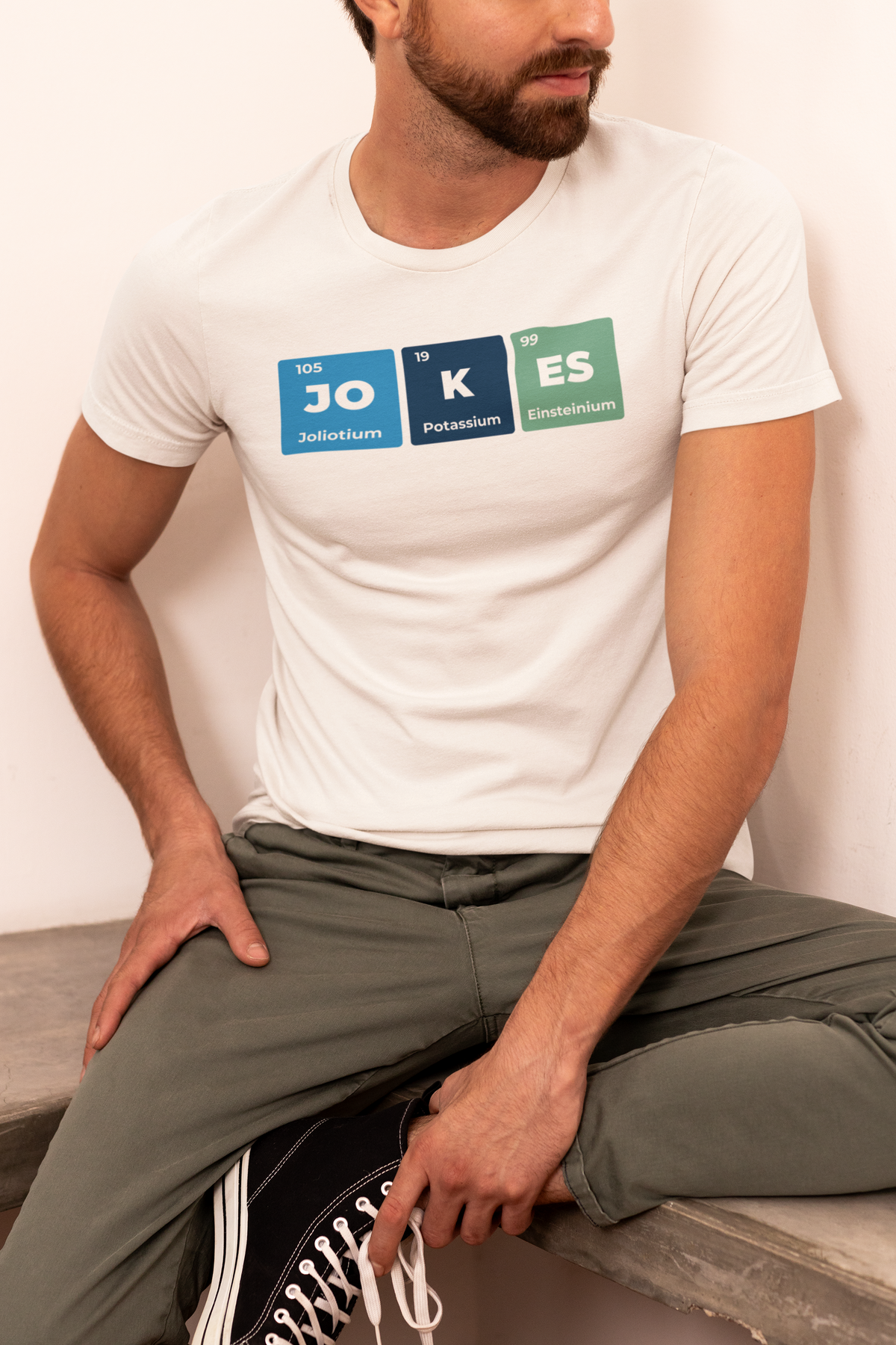 'Jokes' periodic table t-shirt in cream, man sitting outdoors wearing it, funny science pun gift