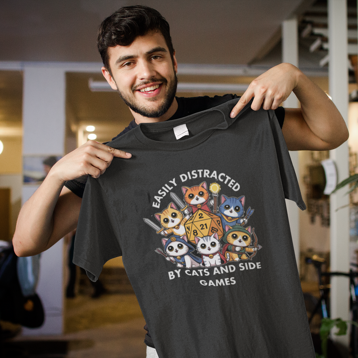 'Easily Distracted by Cats and Side Games' t-shirt in charcoal, man holding it up smiling, funny gift for gamers