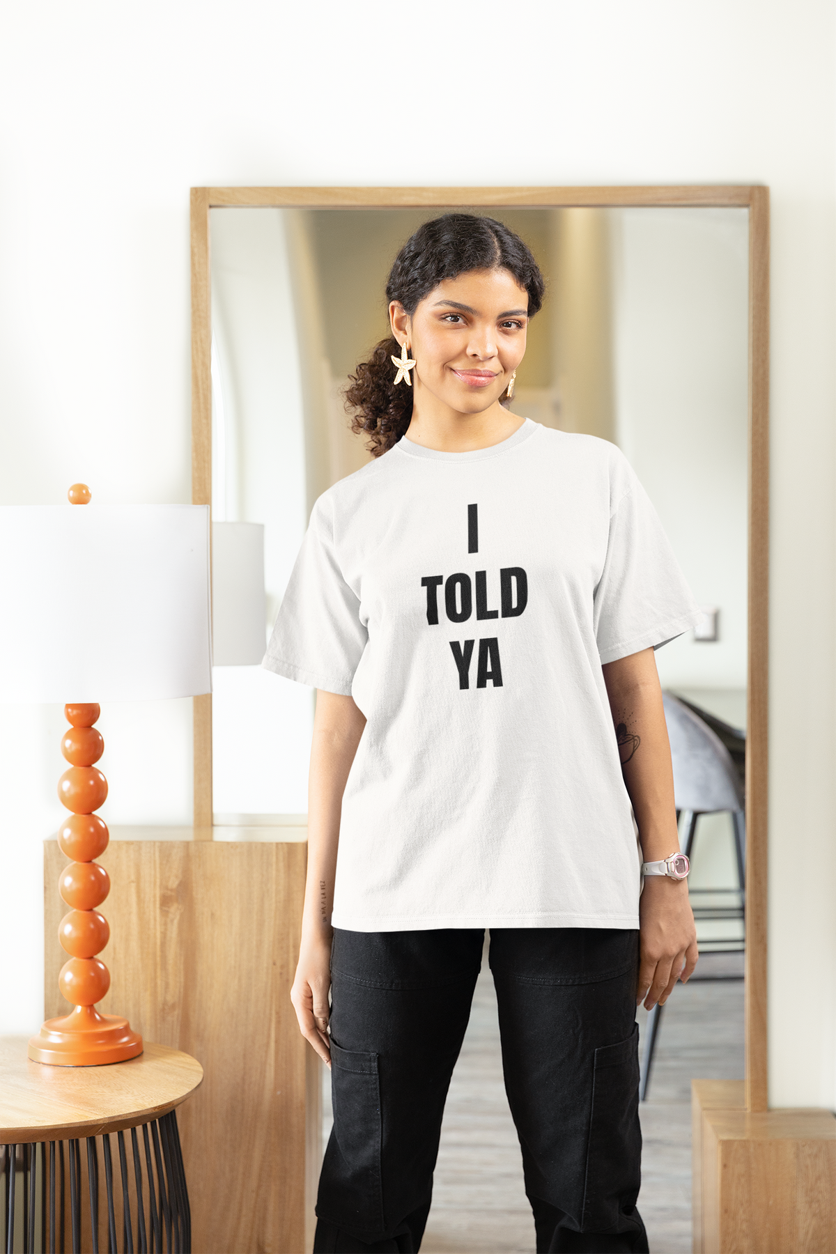 "I Told Ya" quote t-shirt in white, woman wearing it in a cozy living room, funny sarcastic tee