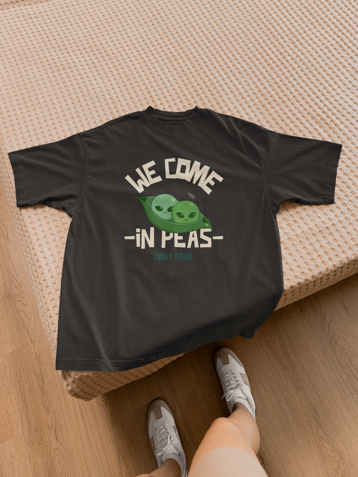 We Come in Pees T-Shirt in black, flat lay on wood floor, funny alien pea pun graphic tee
