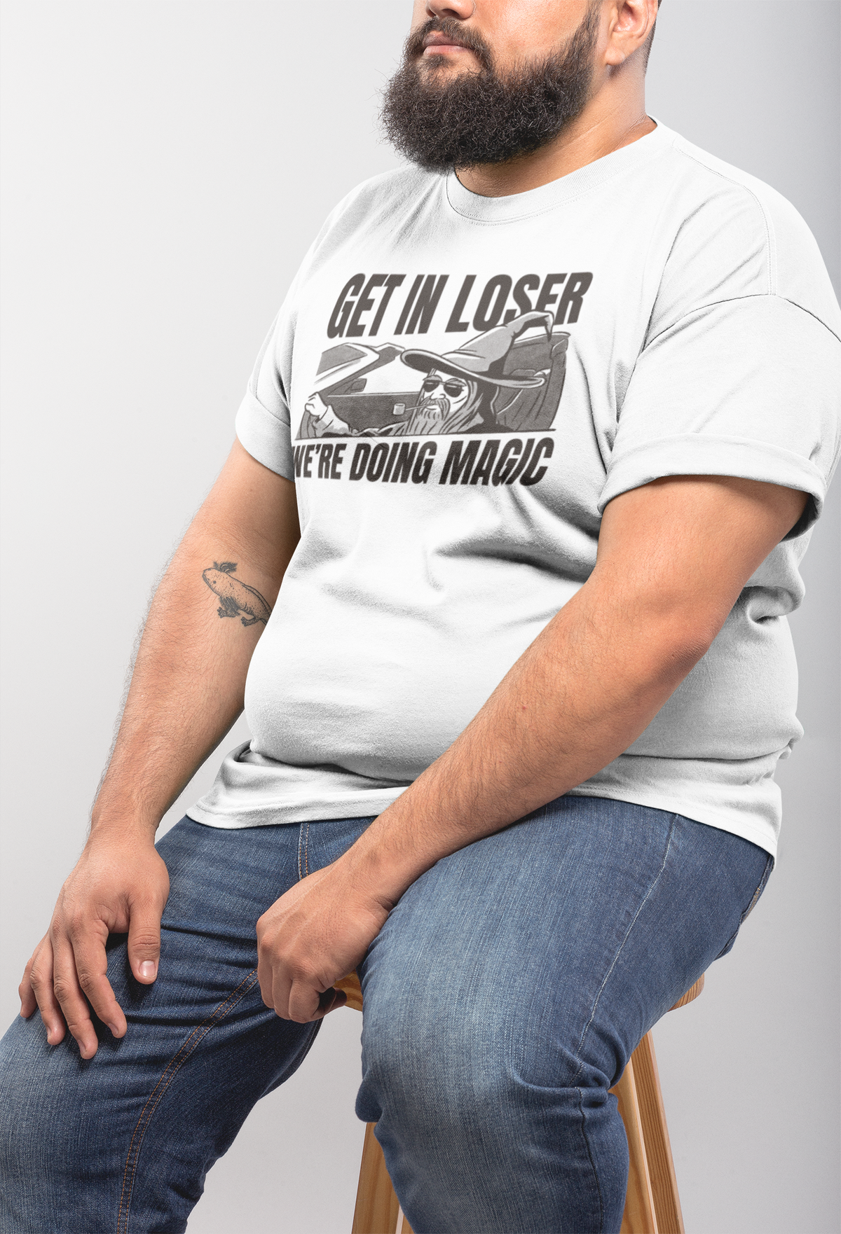 'Get In Loser, We're Doing Magic' t-shirt in white, heavyset man model seated wearing it