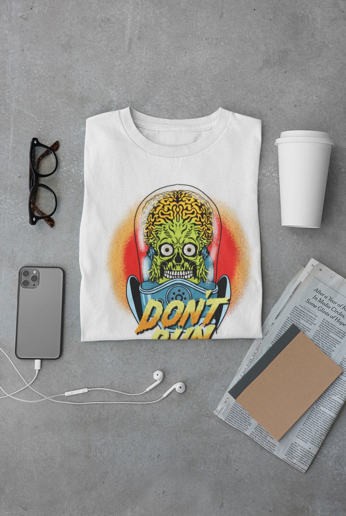 Don't Run alien tee in white, flat lay on concrete with glasses, phone and coffee, sci-fi gift