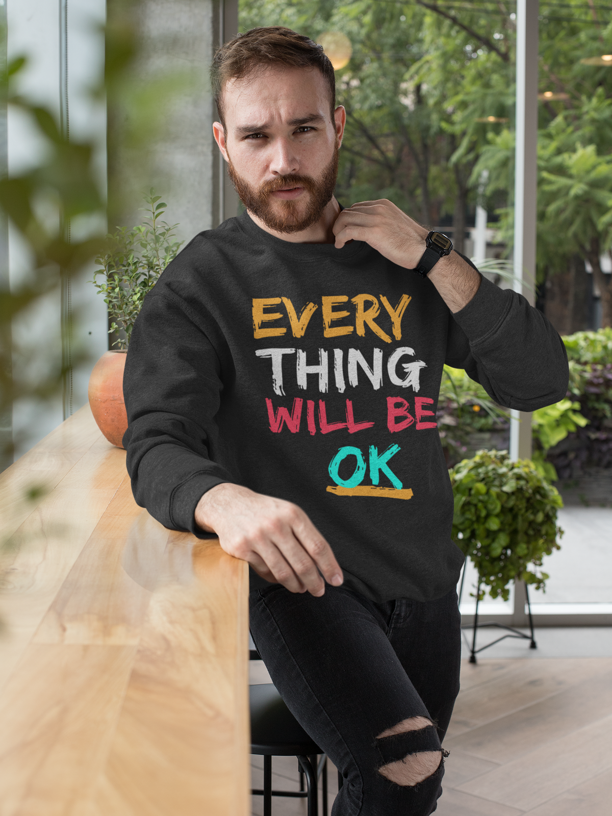 'Everything Will Be OK' sweatshirt in black, bearded man wearing it outdoors, motivational gift