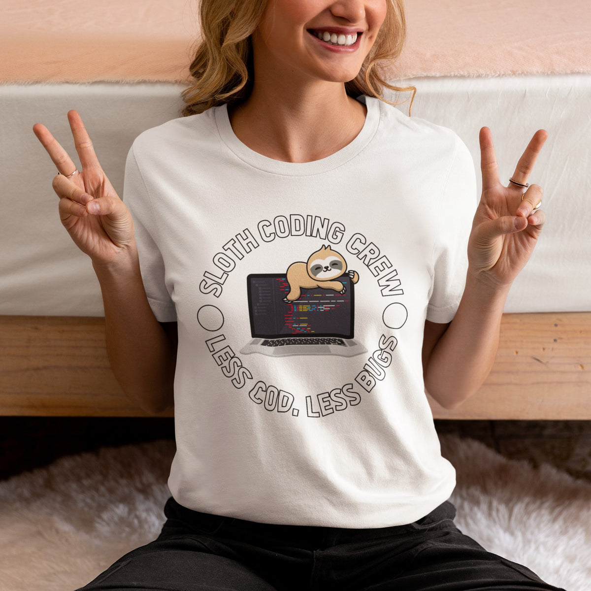 Sloth Coding Crew tee in cream, woman making peace signs on a bed, funny programmer gift