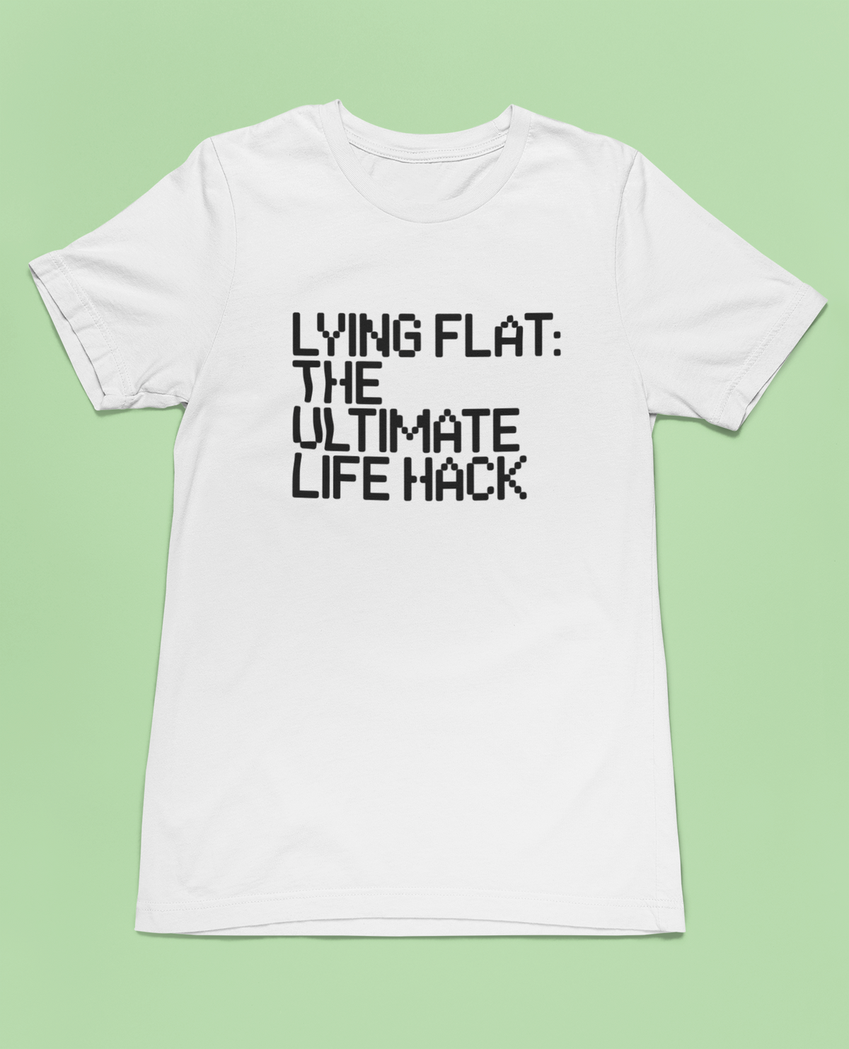 'Lying Flat: The Ultimate Life Hack' t-shirt in white, flat lay on green background, funny gift for procrastinators