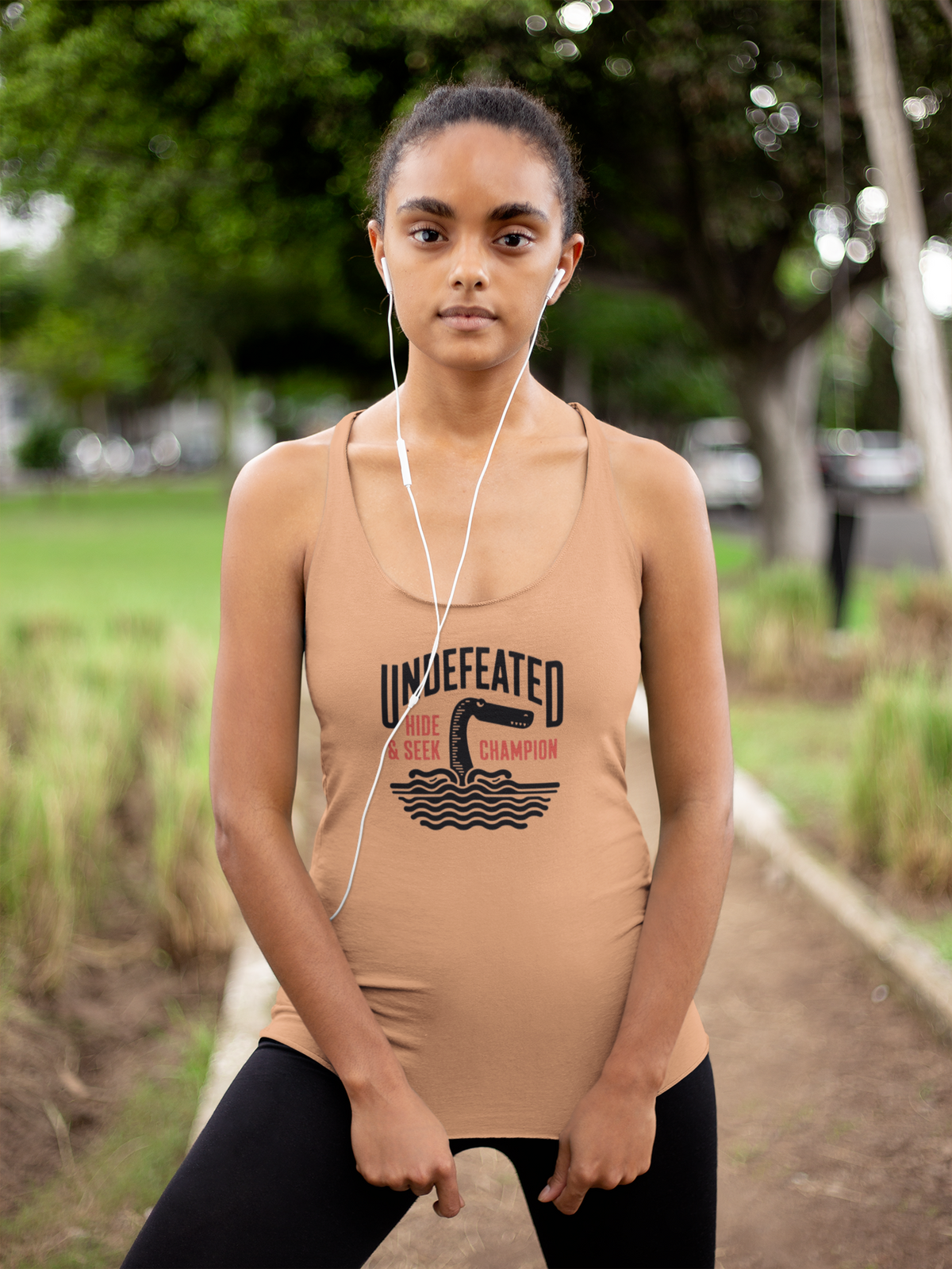 'Undefeated Hide and Seek Women's Tank' in light orange, woman in a park, Tank Top mockup, Geekpsters