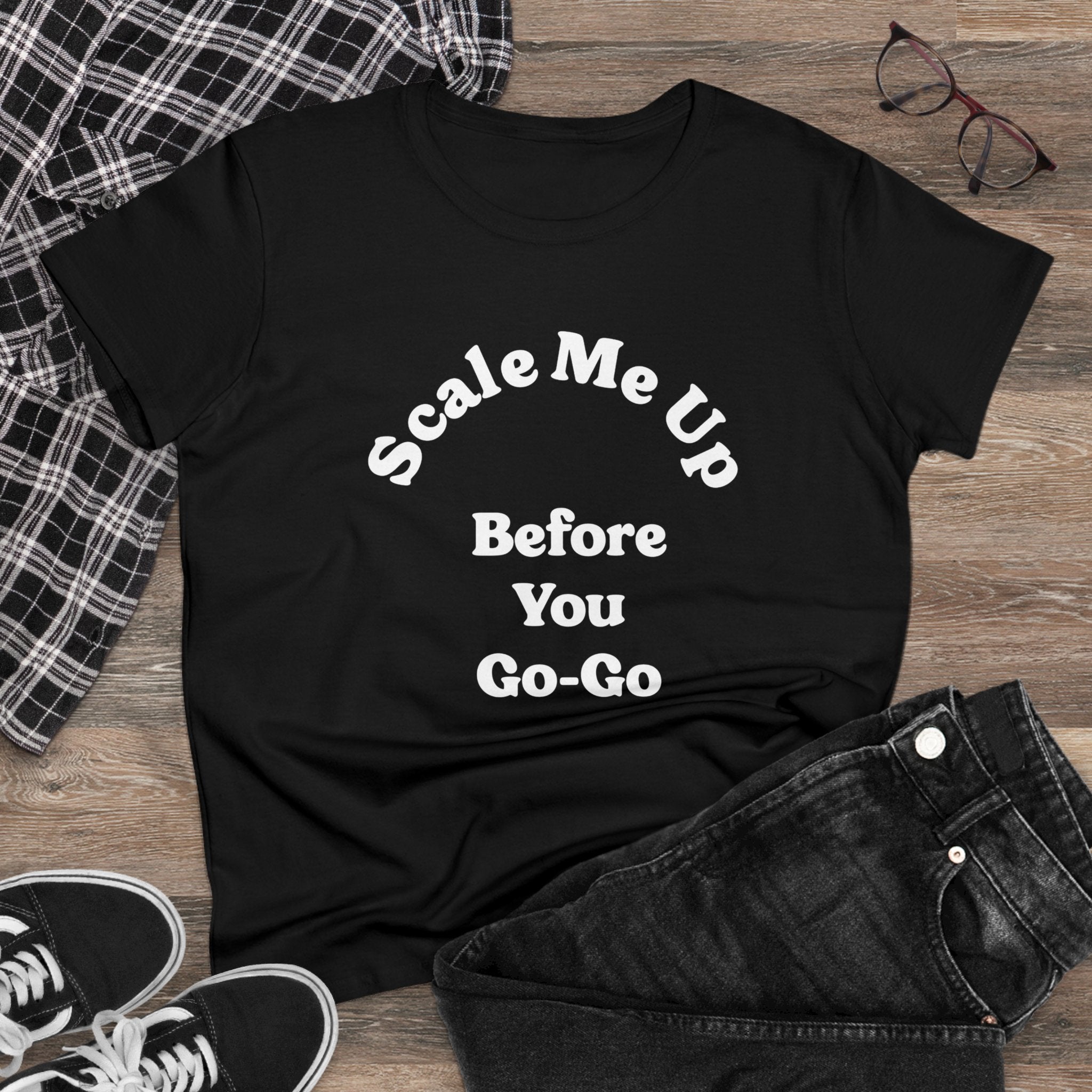 The Scale Me Up Before You Go Go - Women's Tee is adorned with playful white text, perfectly styled with black jeans, a plaid shirt, and glasses on a wooden floor—ideal for anyone who loves fun fashion.