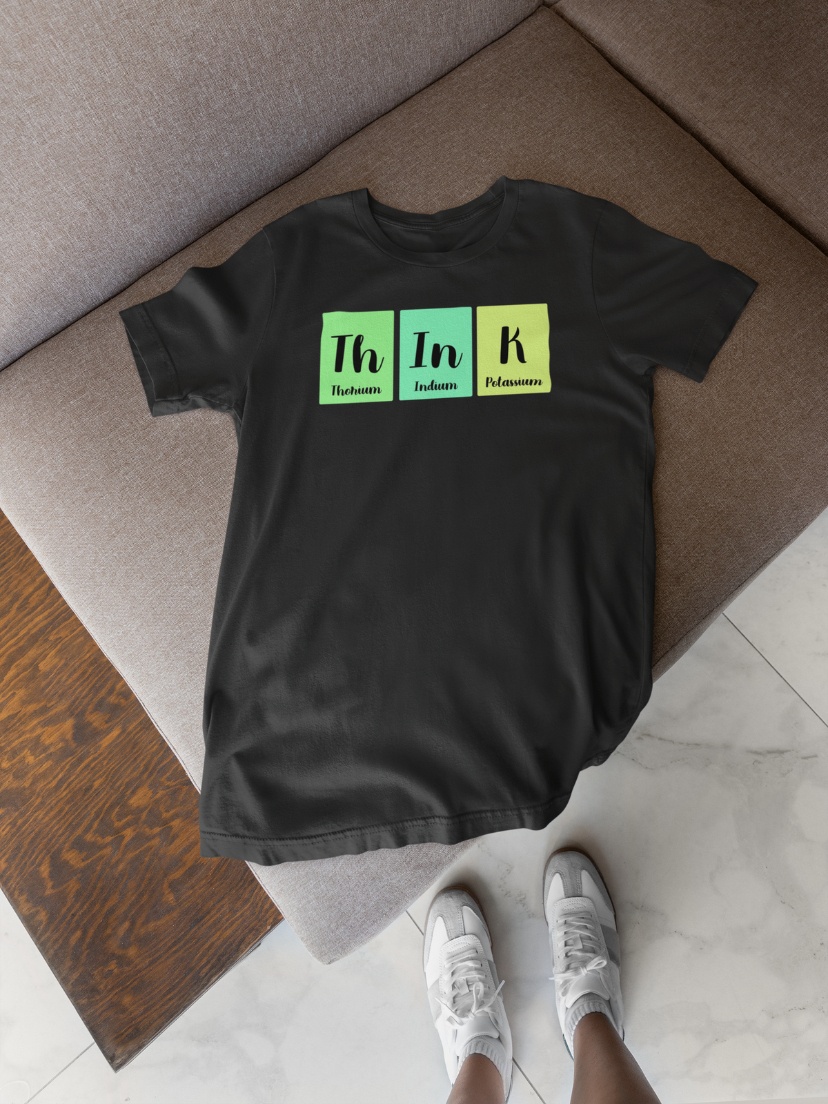'Think' periodic table t-shirt in black, flat lay on wood floor with shoes, funny science pun gift for smart thinkers