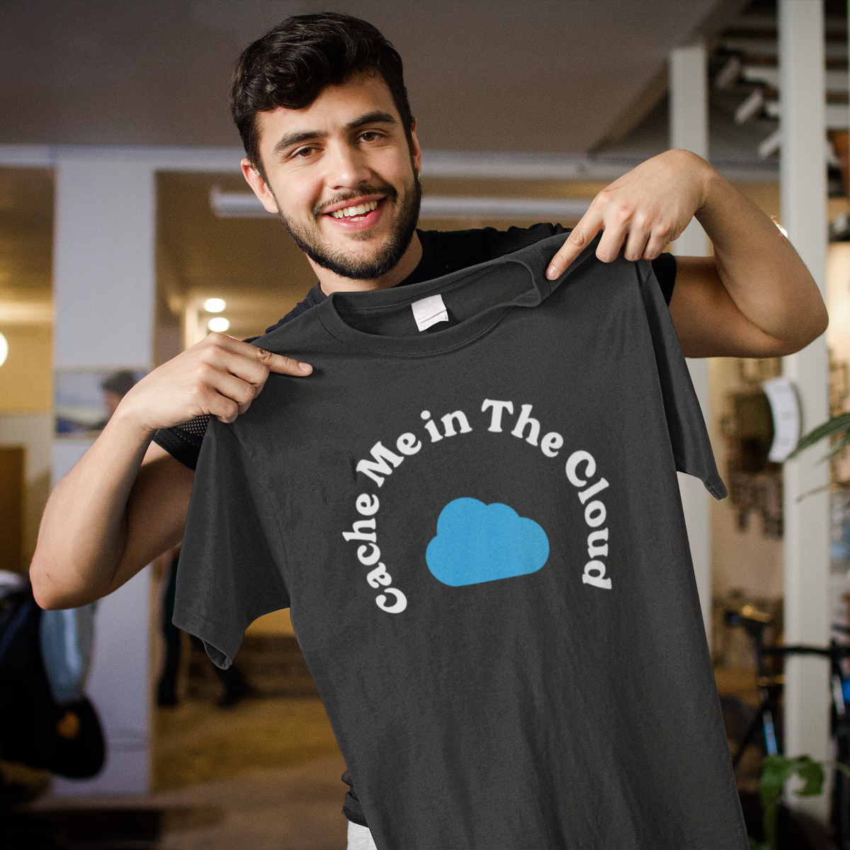 'Cache Me in The Cloud' t-shirt in black, smiling man holding up the shirt indoors, funny gift for developers