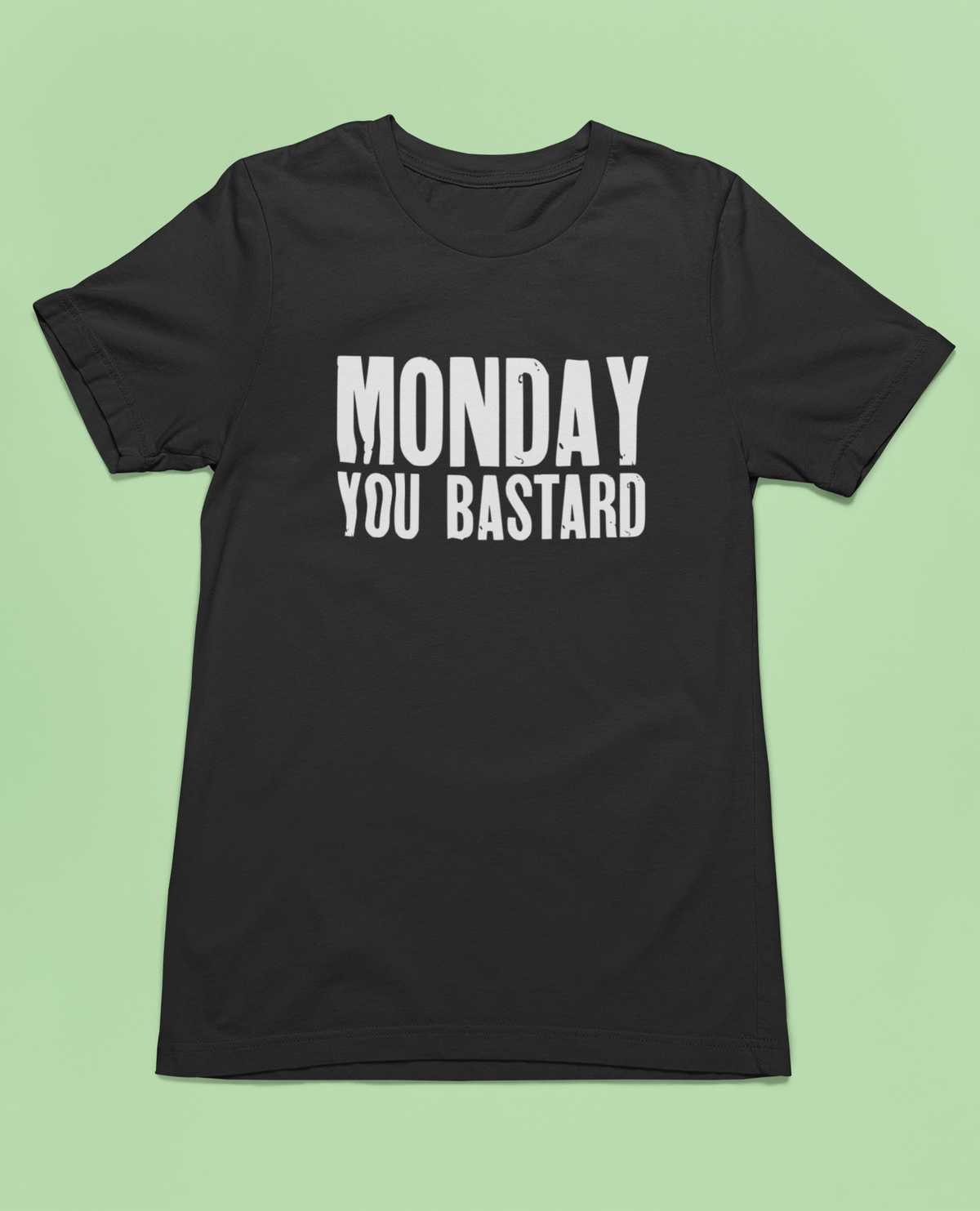 'Monday You Bastard' t-shirt in black, flat lay on pale green background, funny anti-Monday gift