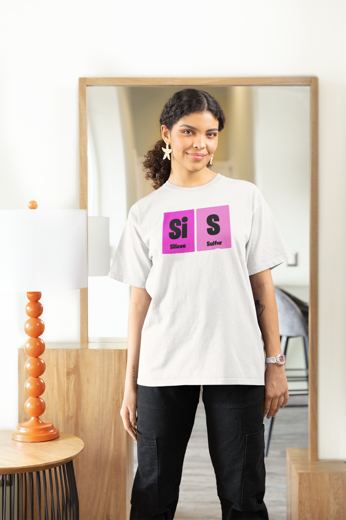 'Sis' periodic table women's tee in white, woman standing at home, casual lifestyle photo