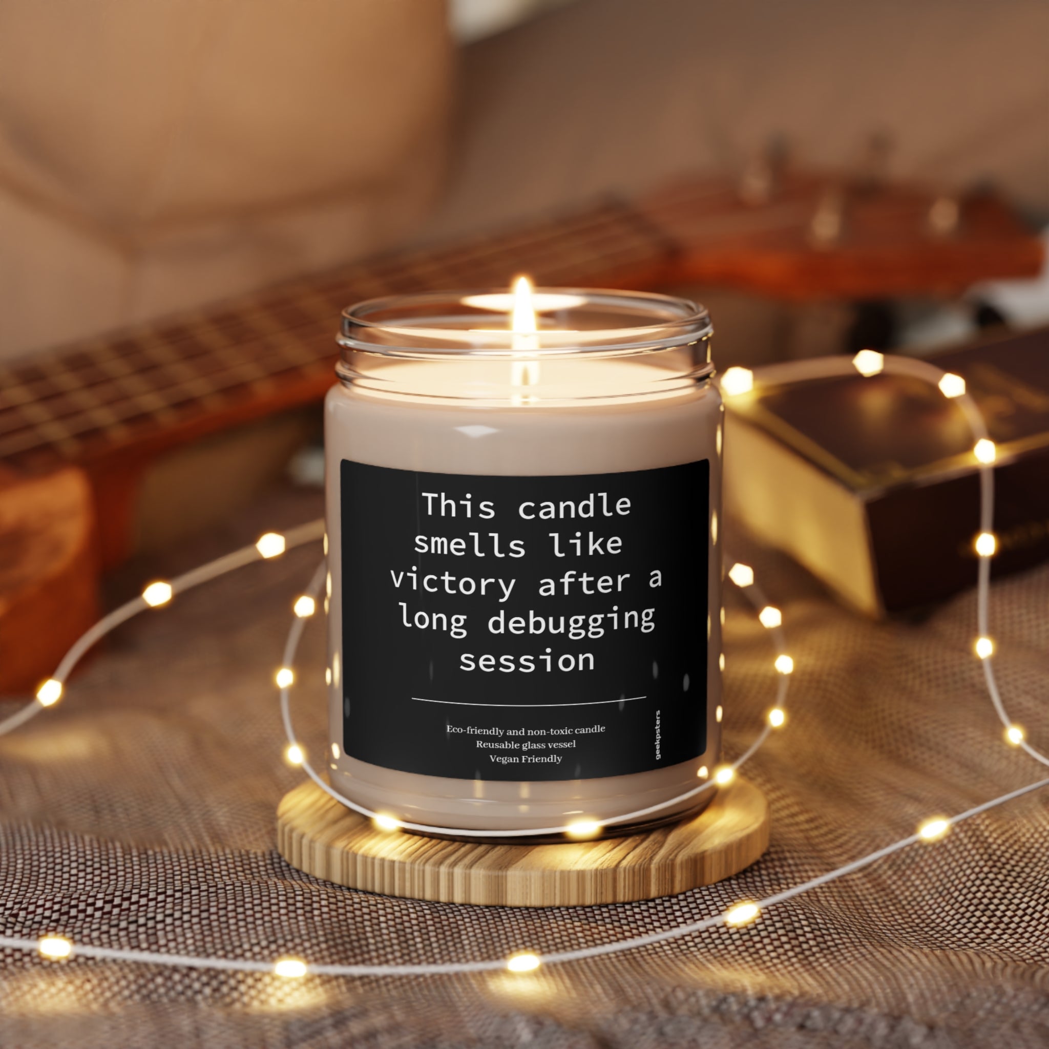 A lit This Candle Smells Like Victory After a Long Debugging Session - Scented Soy Candle, 9oz with a label reading "this candle smells like victory after a long debugging session" on a wooden holder, surrounded by small lights.