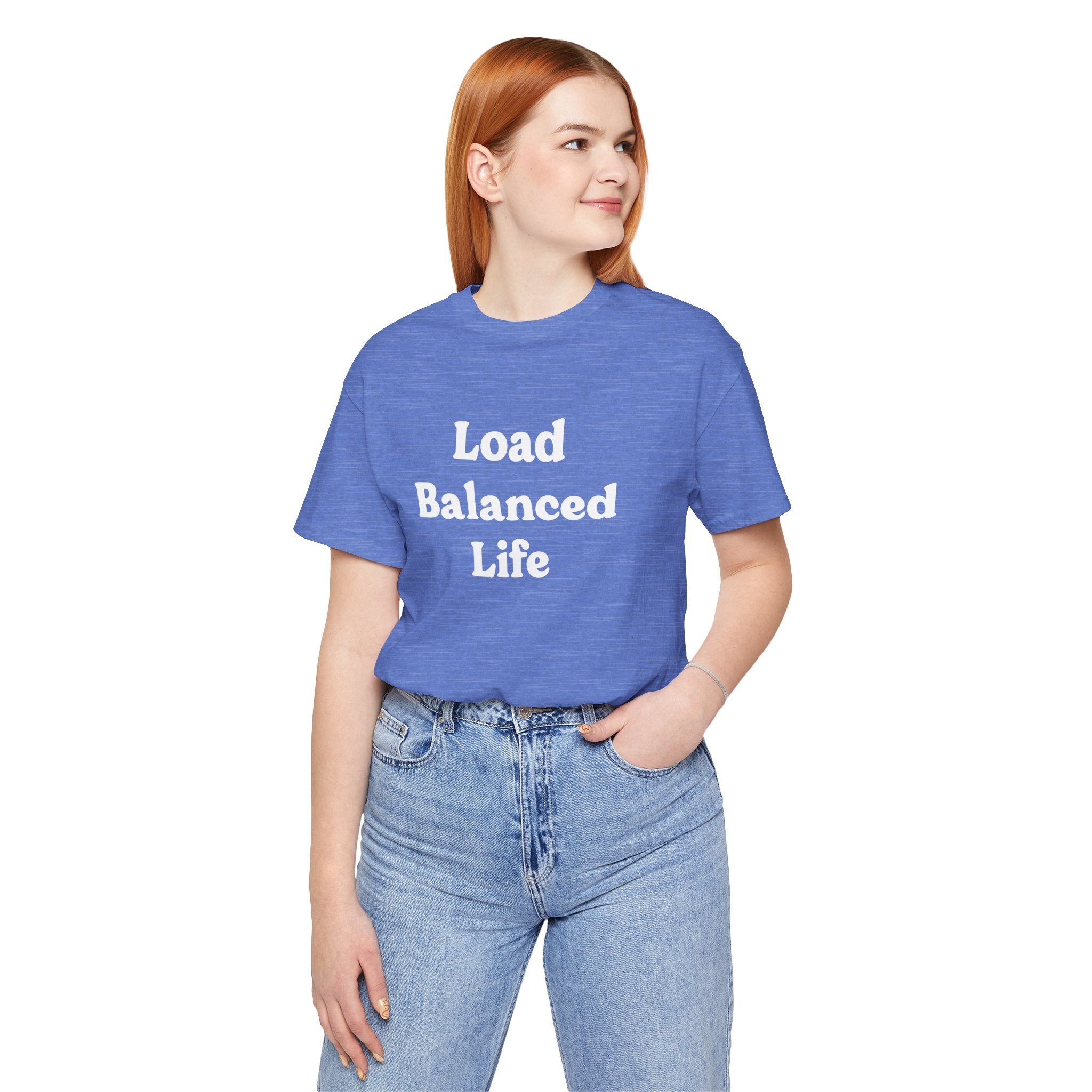 A person with red hair stands smiling, wearing the "Load Balanced Life" t-shirt in blue. Made from Airlume combed and ring-spun cotton, it provides exceptional comfort and is complemented by light blue jeans.