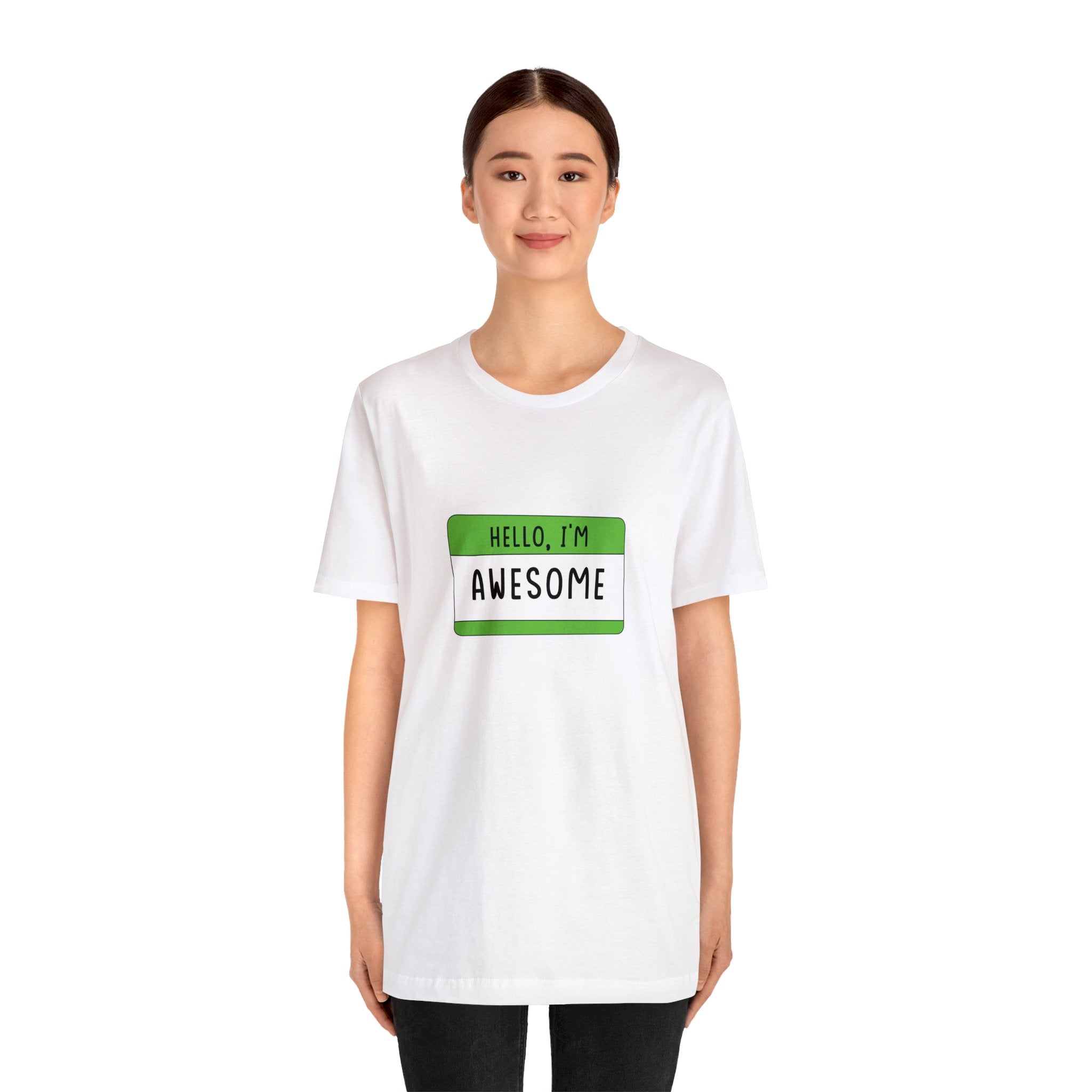 Young woman wearing a Hello, I'm Awesome T-Shirt with a green name tag that says "hello, I'm awesome" designed for geeks and gamers, standing against a white background.
